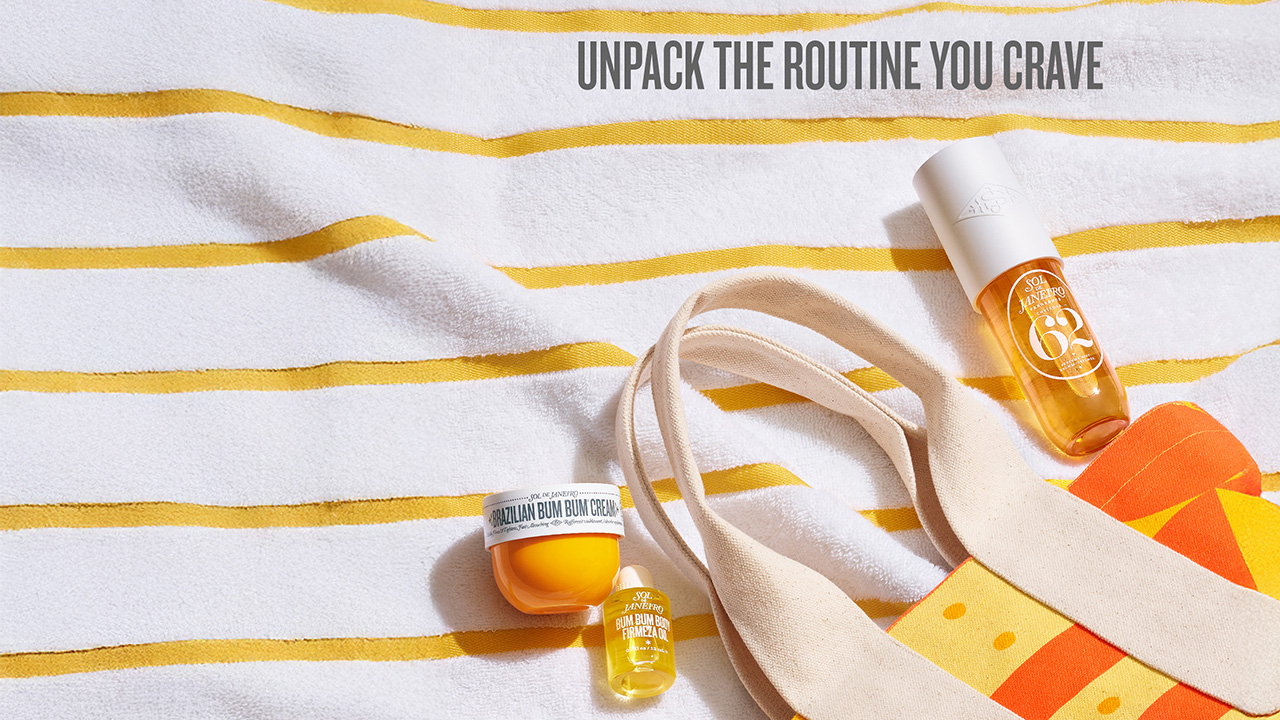Sol de Janeiro products including a body cream and oils are displayed on a striped towel alongside a colorful bag.