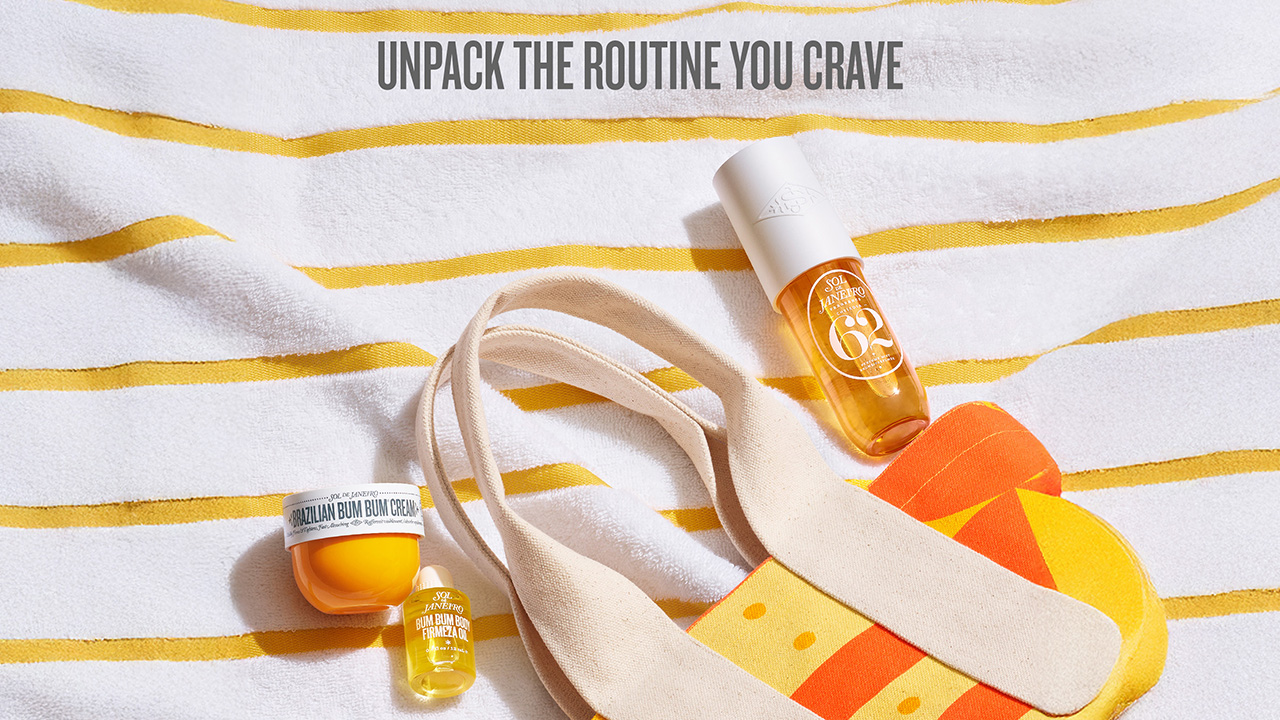 Sol de Janeiro products including a body cream and oils are displayed on a striped towel alongside a colorful bag.