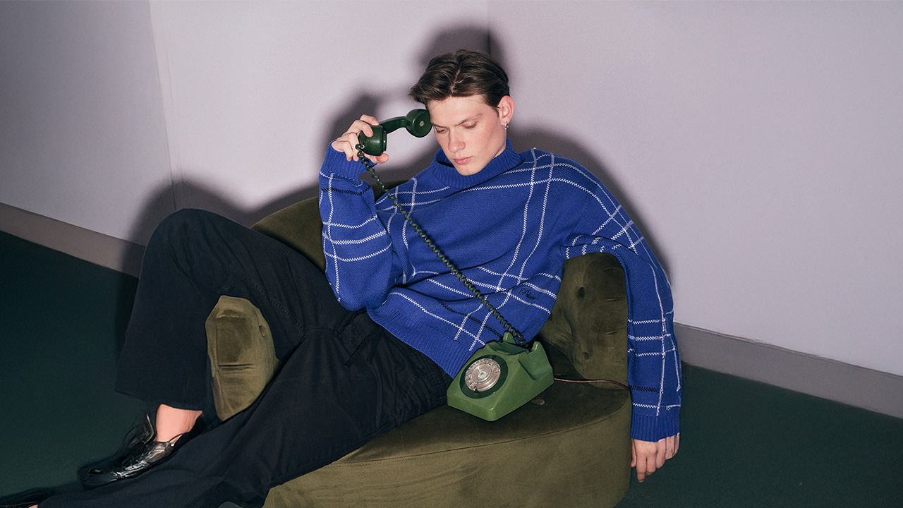 Person in a blue sweater holding a green rotary phone, sitting on an olive green chair.