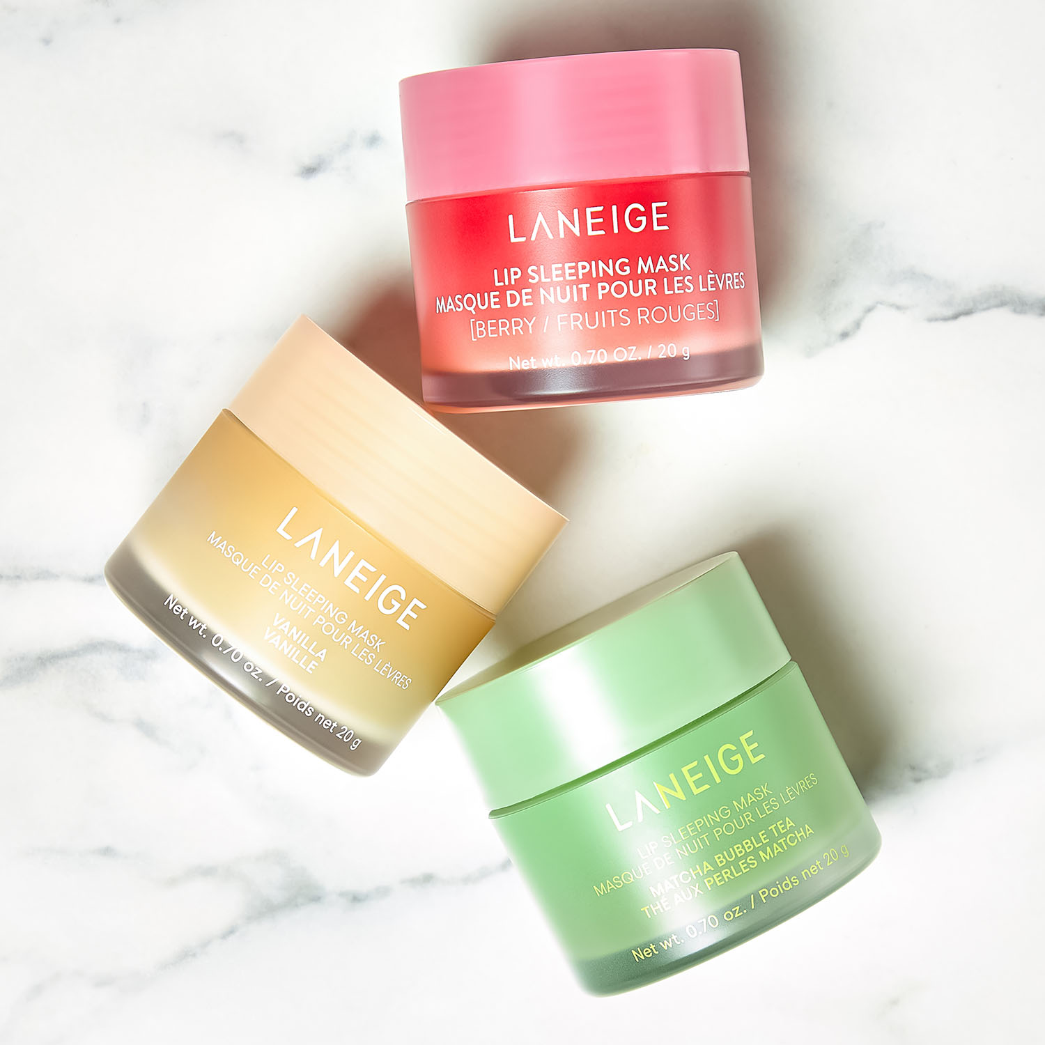 Three Laneige sleeping masks in pink, beige, and green containers on a marble surface.
