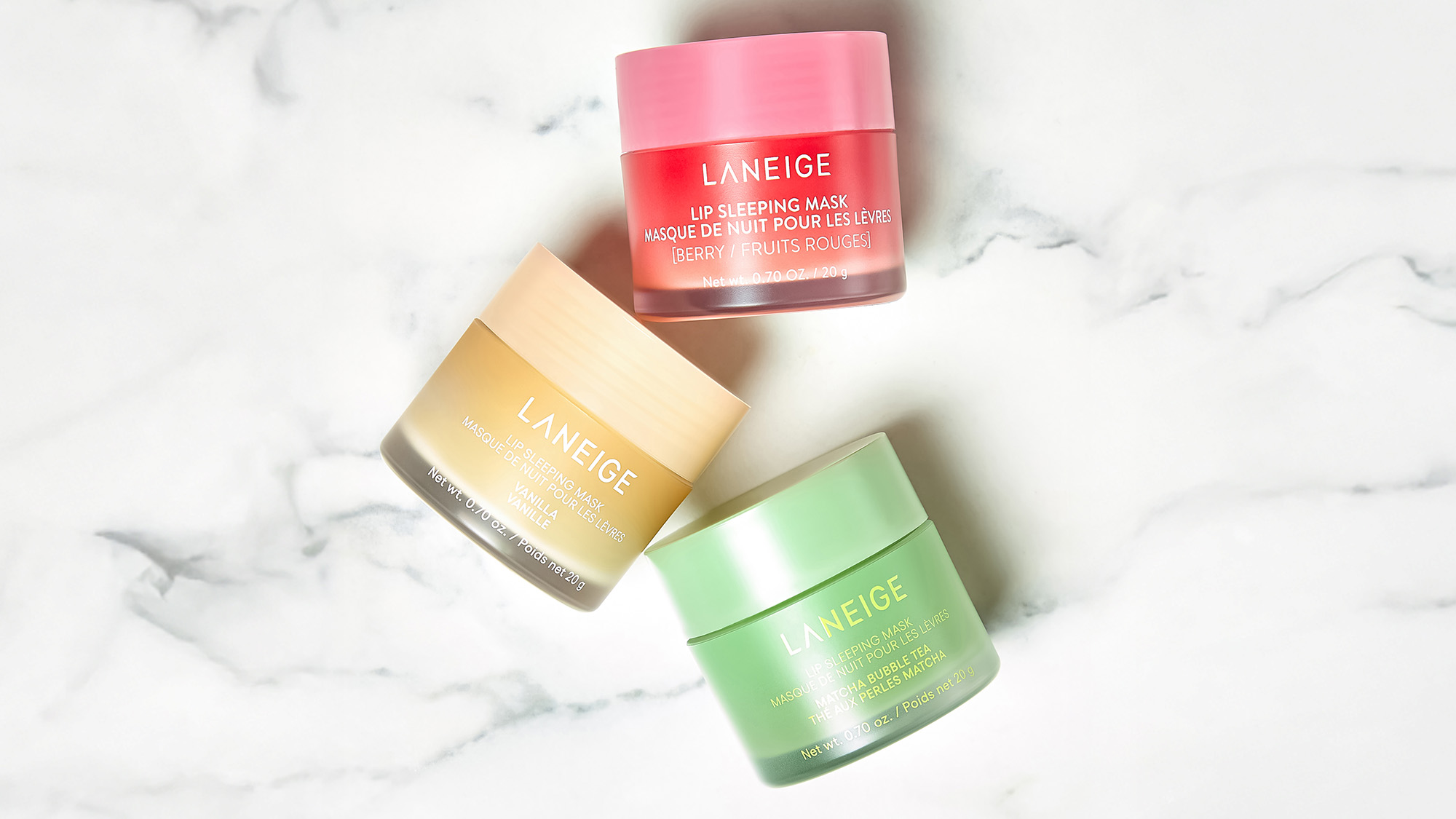 Three LANEIGE lip sleeping mask jars in pink, yellow, and green on a marble surface.