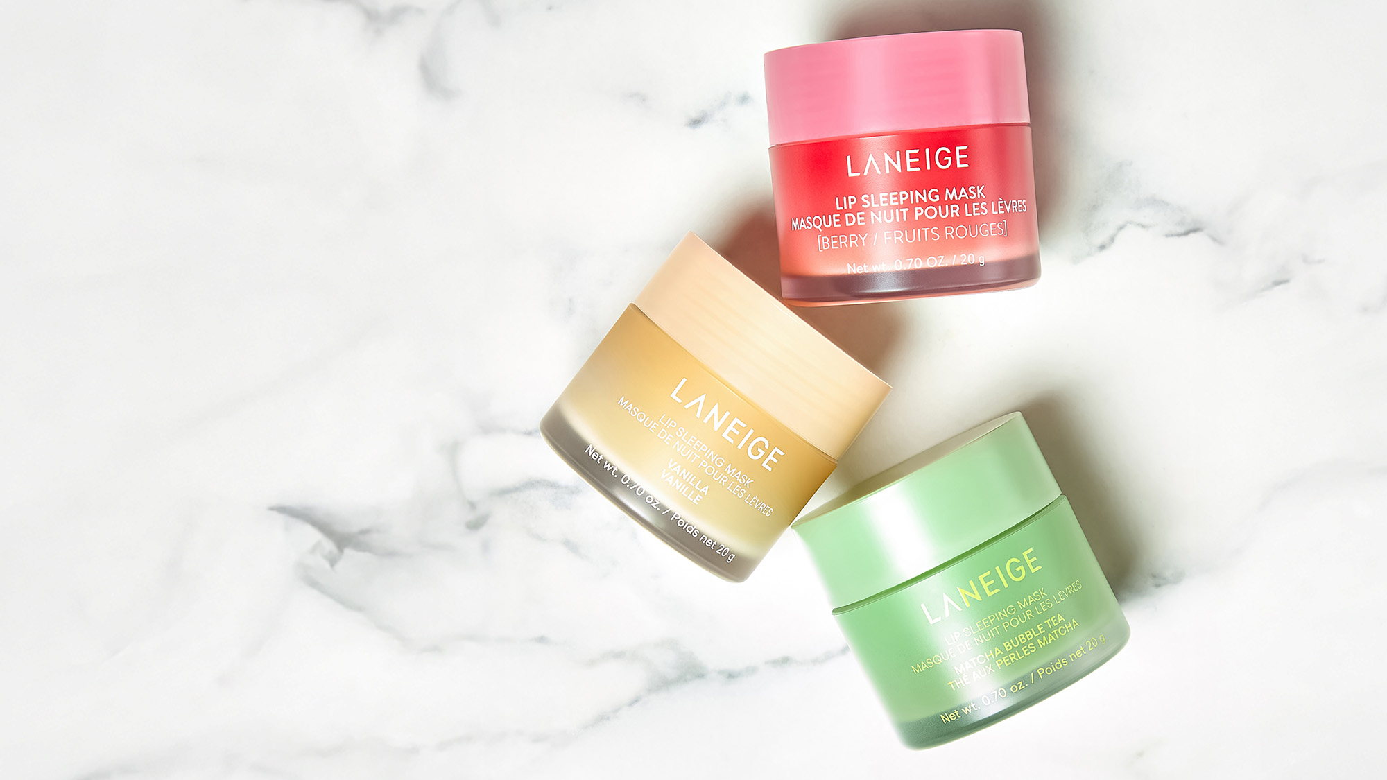 Three LANEIGE lip sleeping mask jars in pink, yellow, and green on a marble surface.