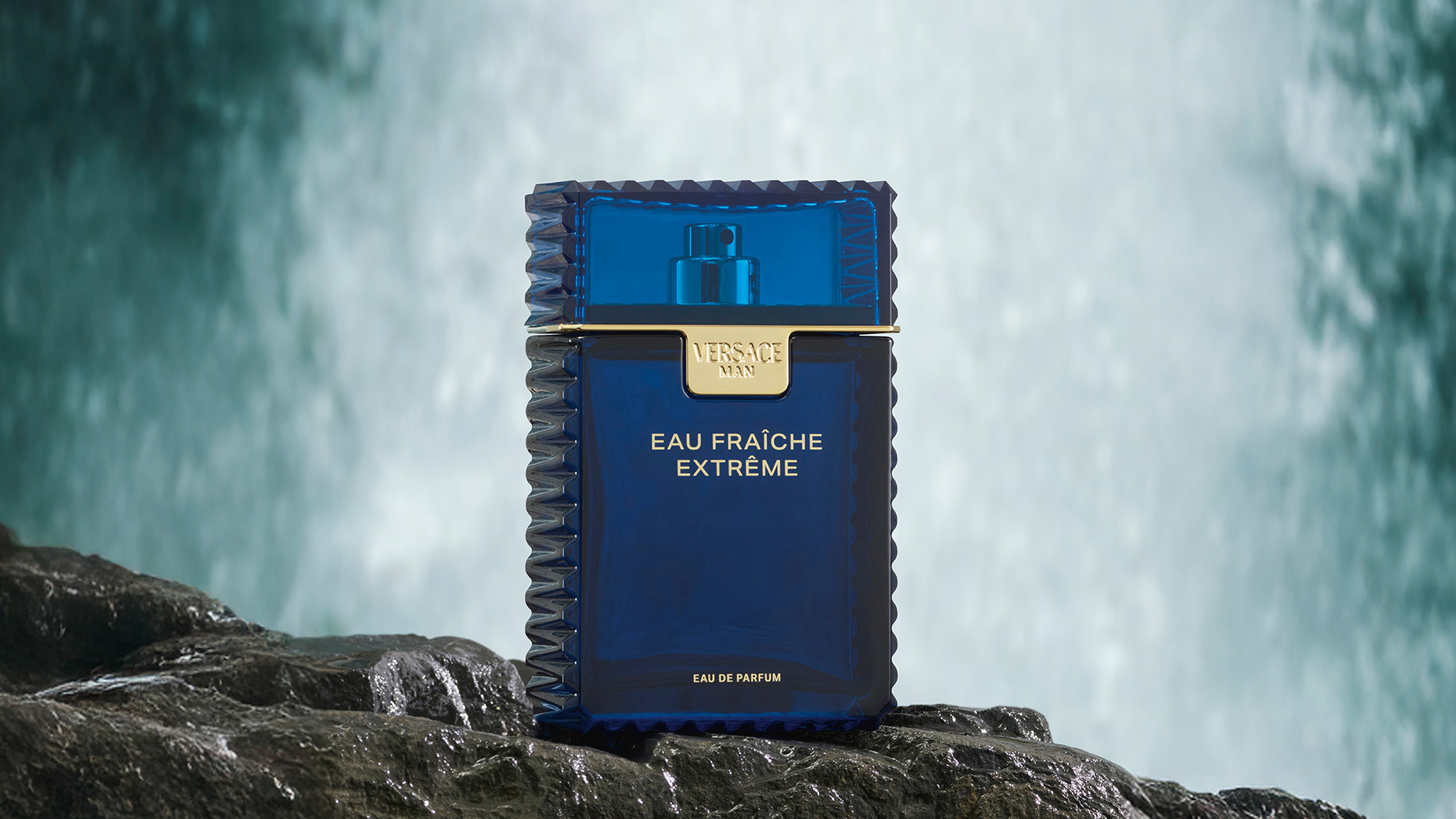 Blue perfume bottle on rocks with a waterfall background.