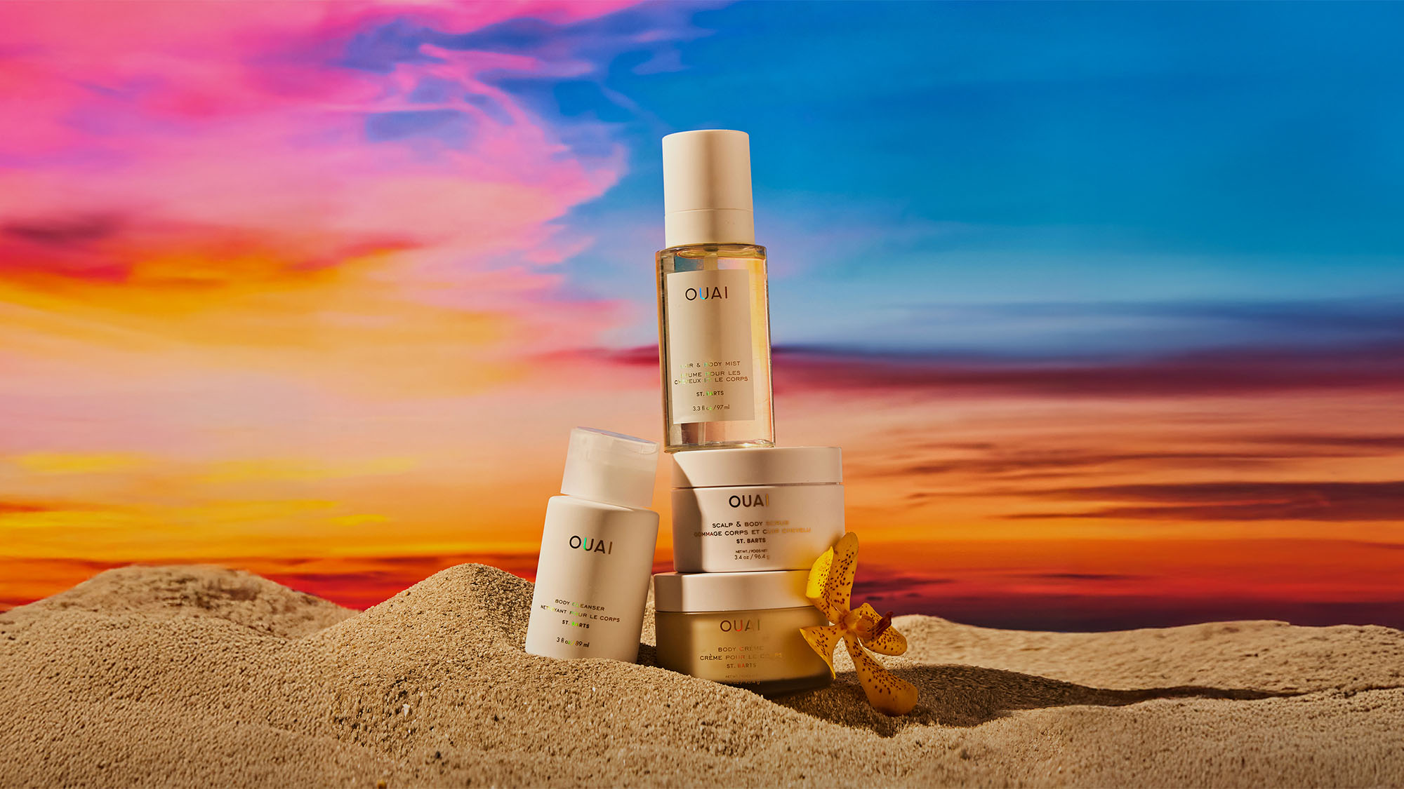 Skincare products displayed on sand with a vivid sunset background.