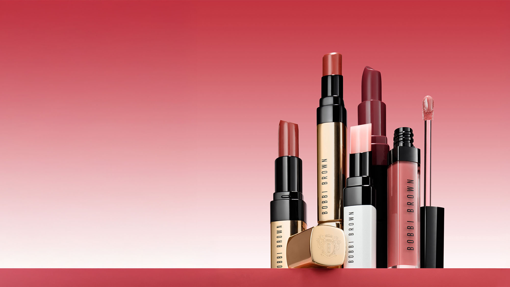 Assorted Bobbi Brown lipsticks and glosses against a red gradient background.