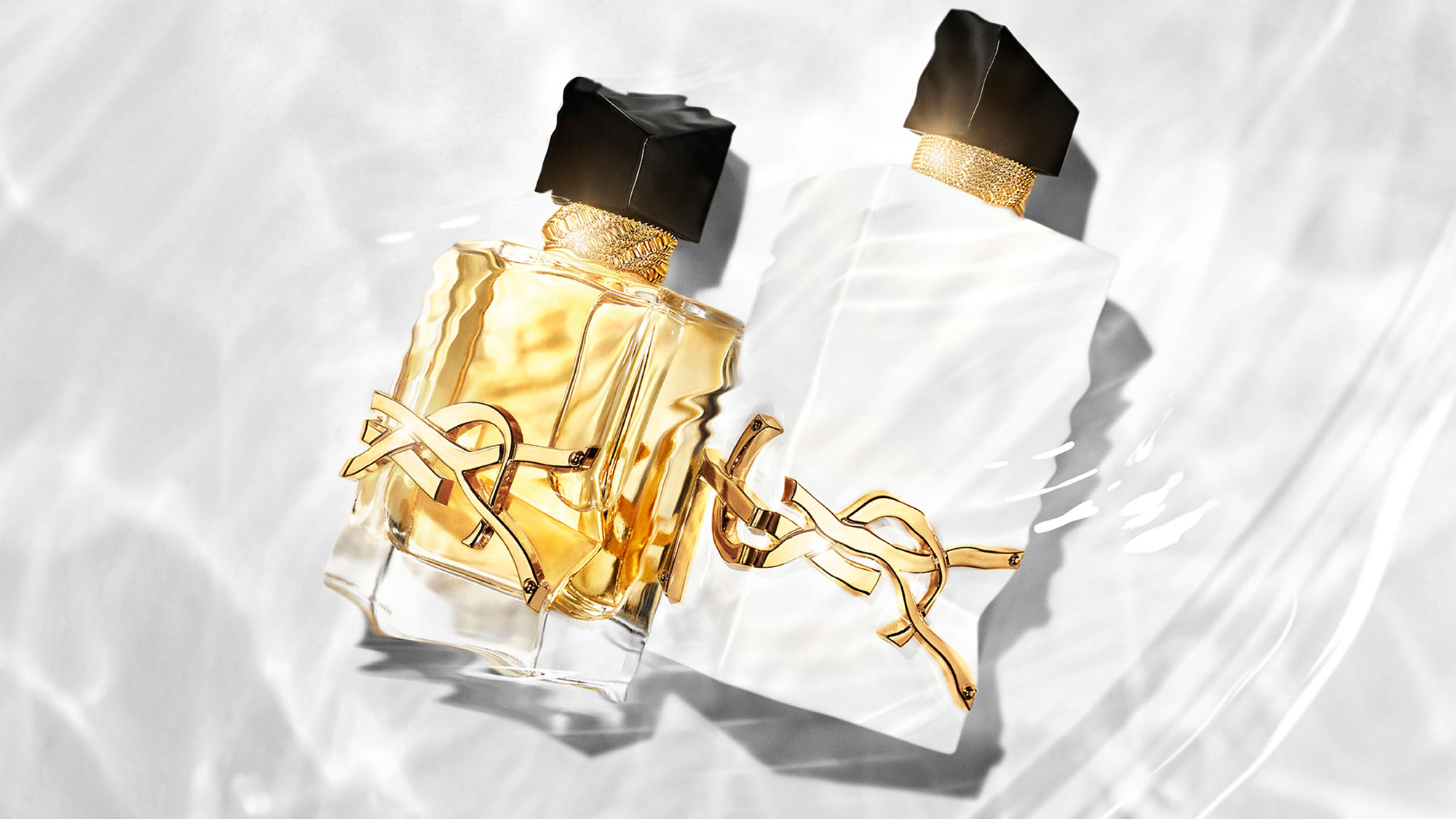 Two elegant perfume bottles with gold accents and black caps on a textured white background.