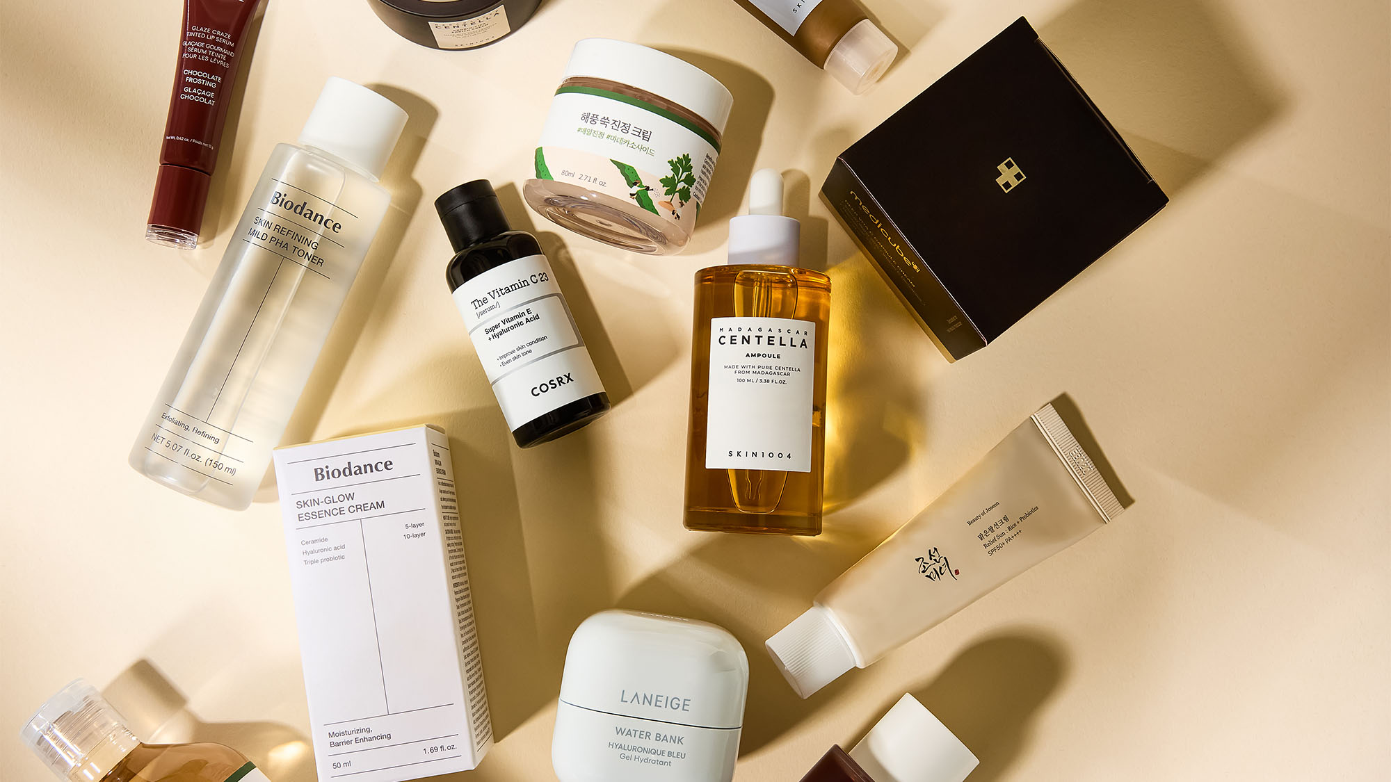 A flat lay of various skincare and cosmetic products on a beige background, including creams, bottles, and boxes.