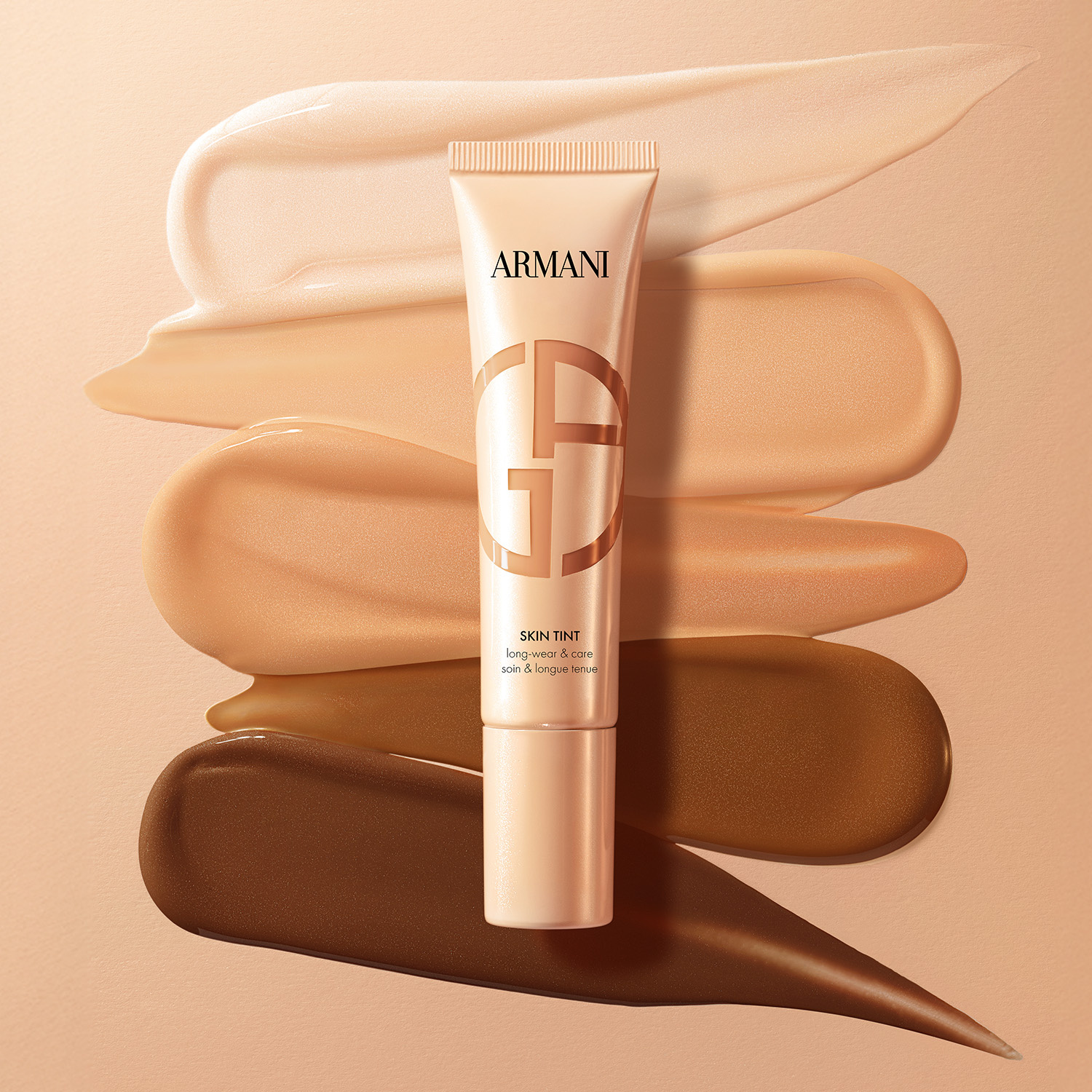 A tube of Armani skin tint is placed over swatches of five different shades on a beige background.