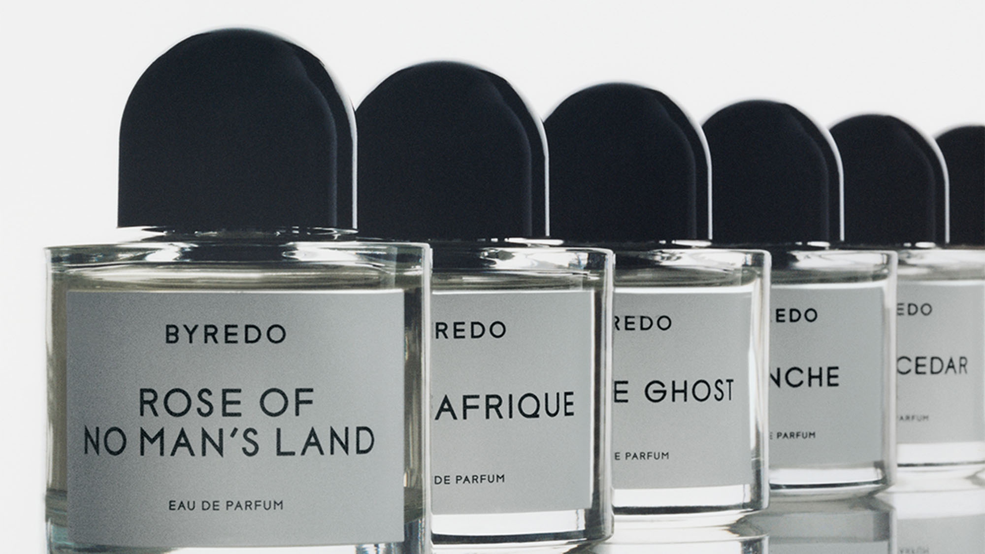 A row of Byredo perfume bottles, each with black caps and labeled with different fragrance names.