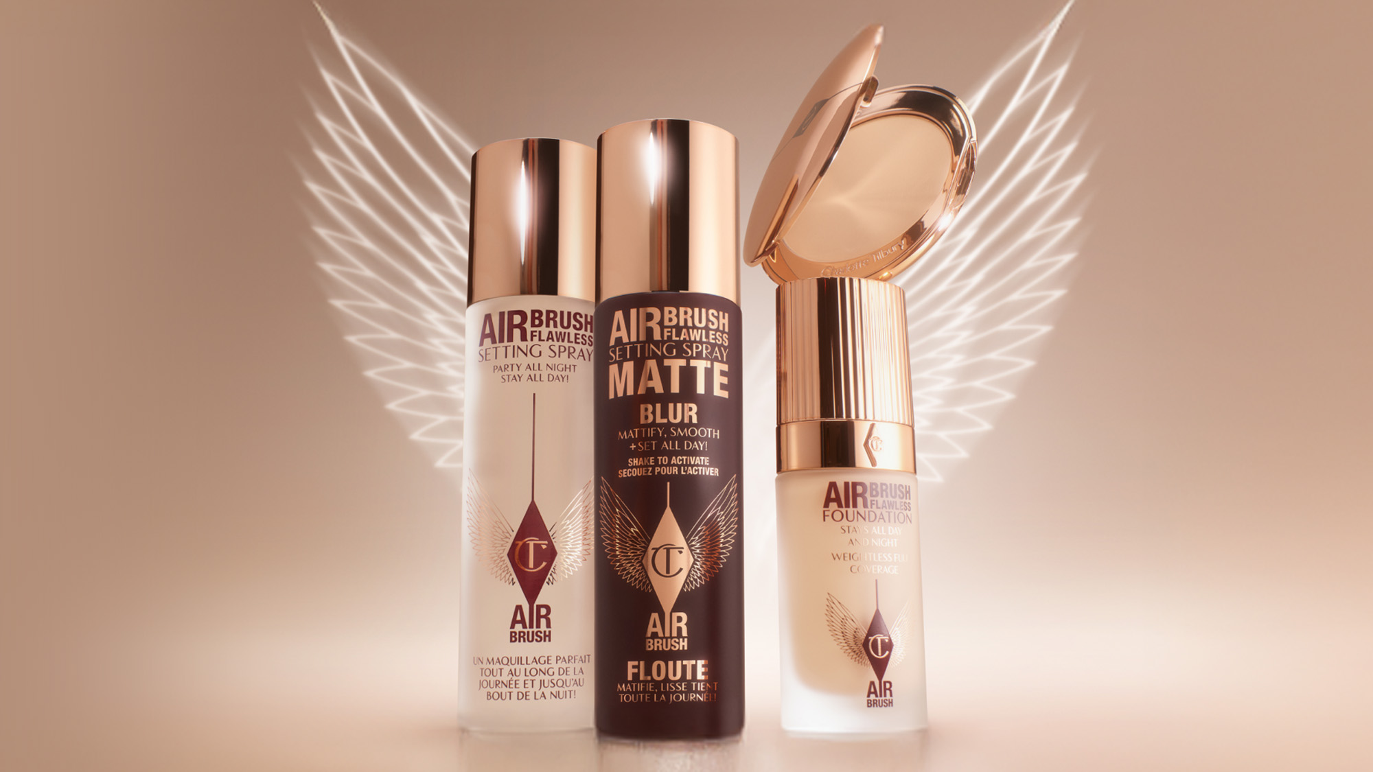 Three makeup products with metallic caps are displayed with white wings in the background on a beige backdrop.
