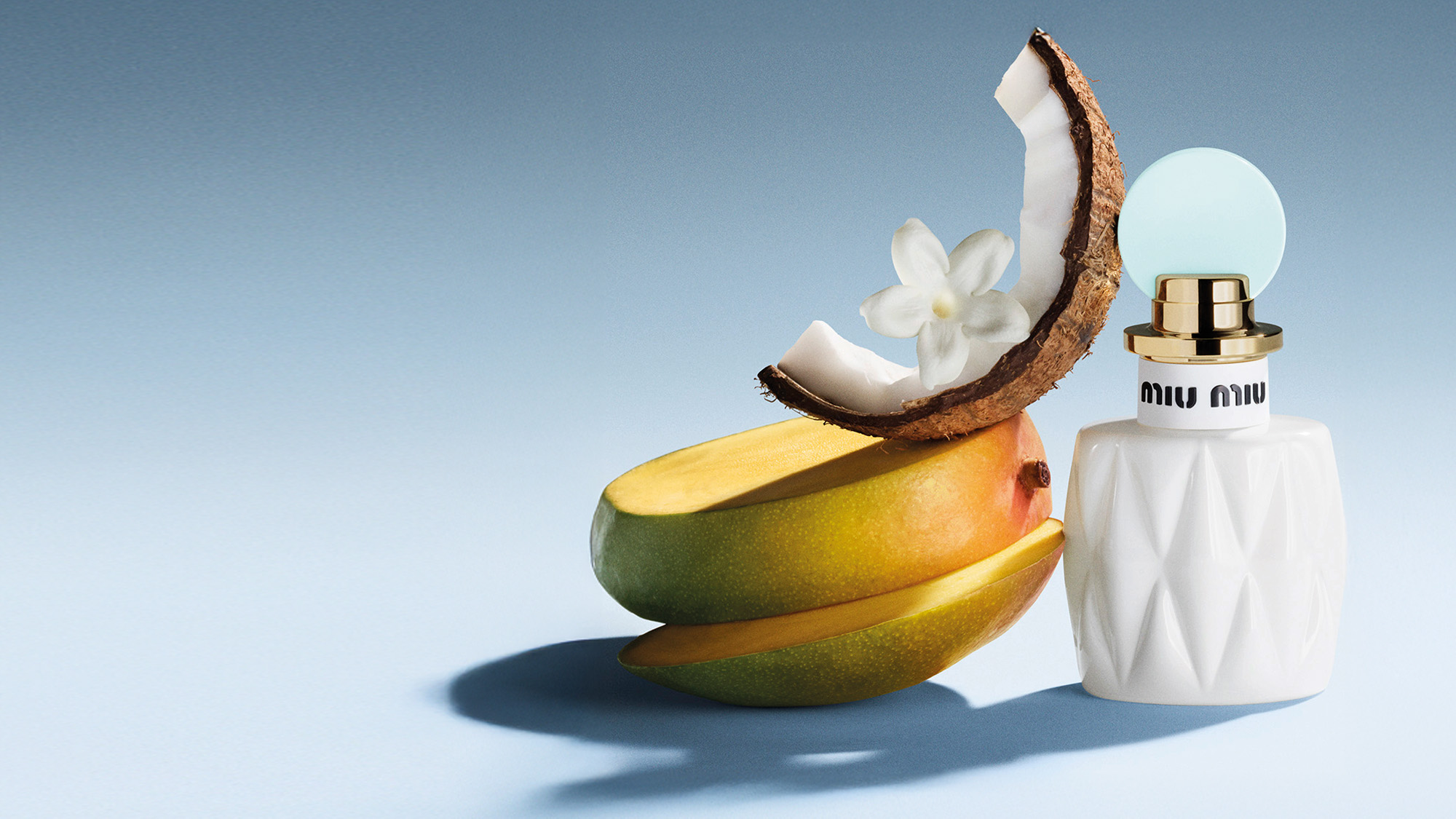 Perfume bottle beside sliced mango and coconut on a blue background.