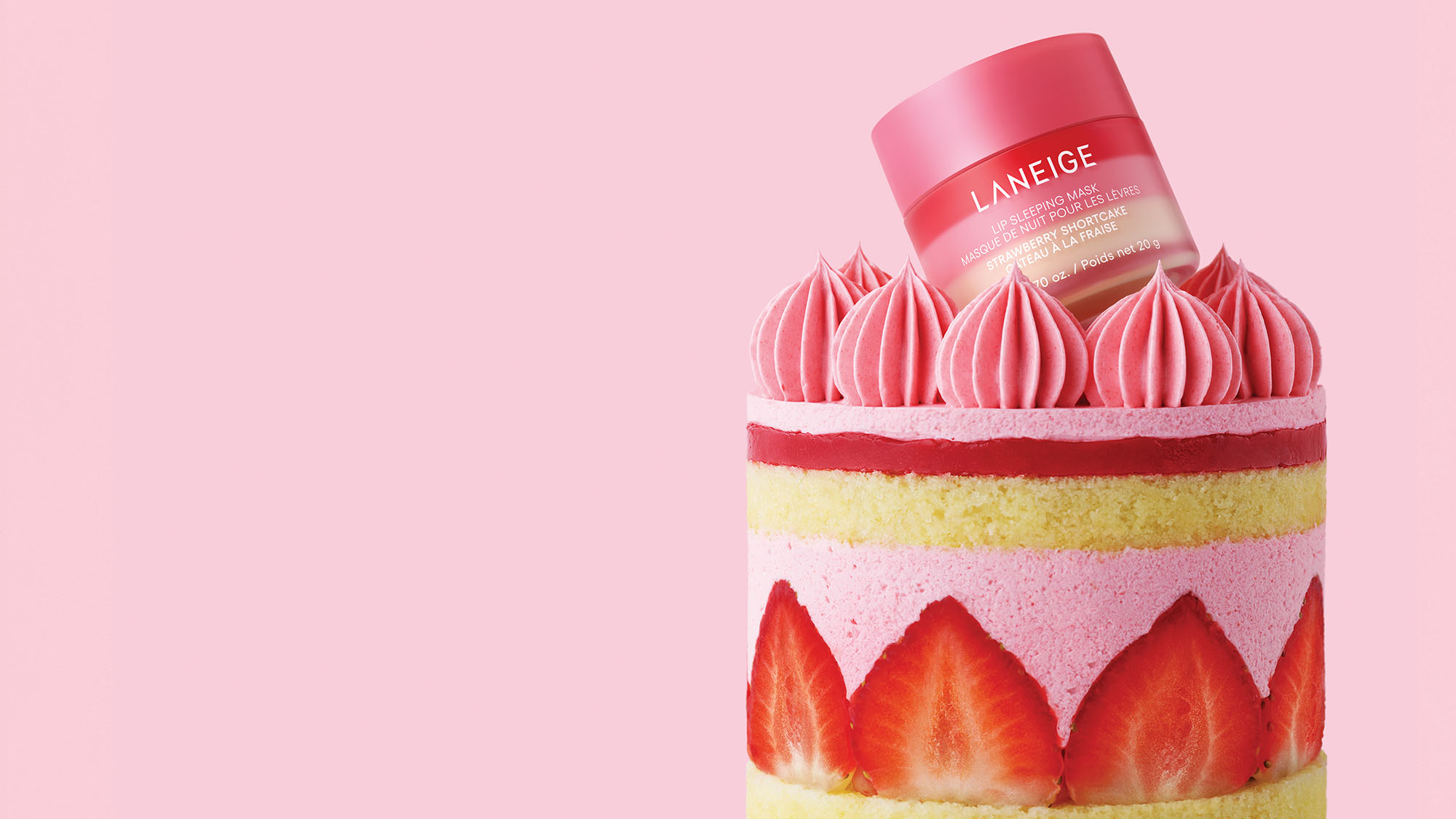 A jar of Laneige lip balm is nestled atop a strawberry and cream-layered cake, set against a light pink background.
