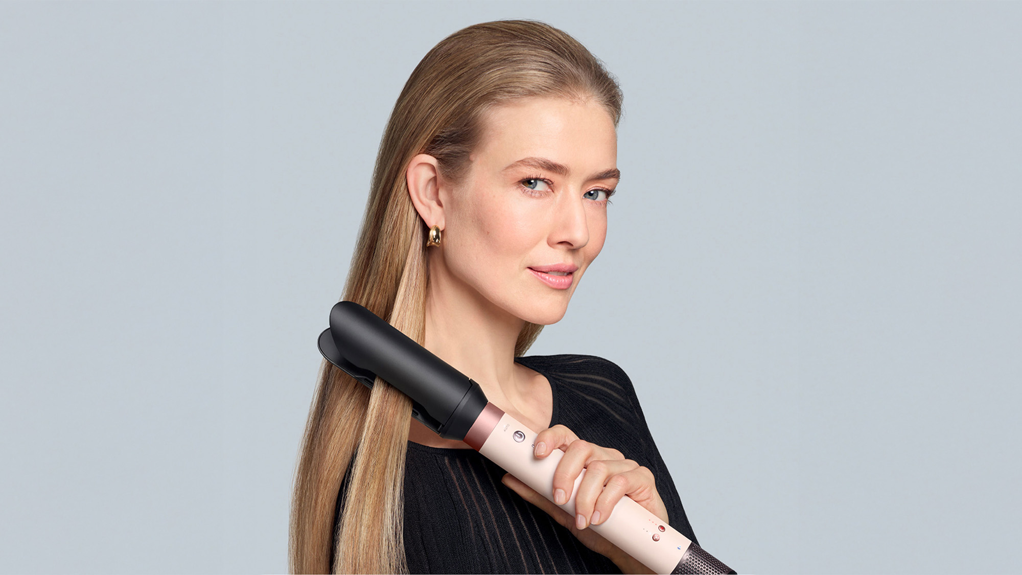 Woman with long blonde hair using a curling iron.