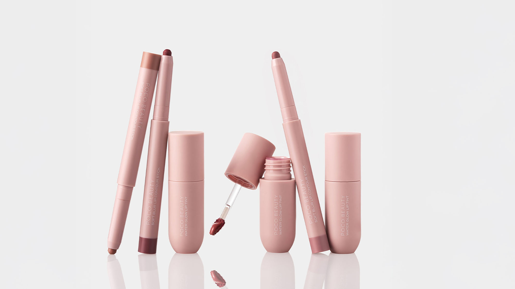 Pink cosmetics, including lip crayons and a lip gloss with an applicator, are arranged against a white background.