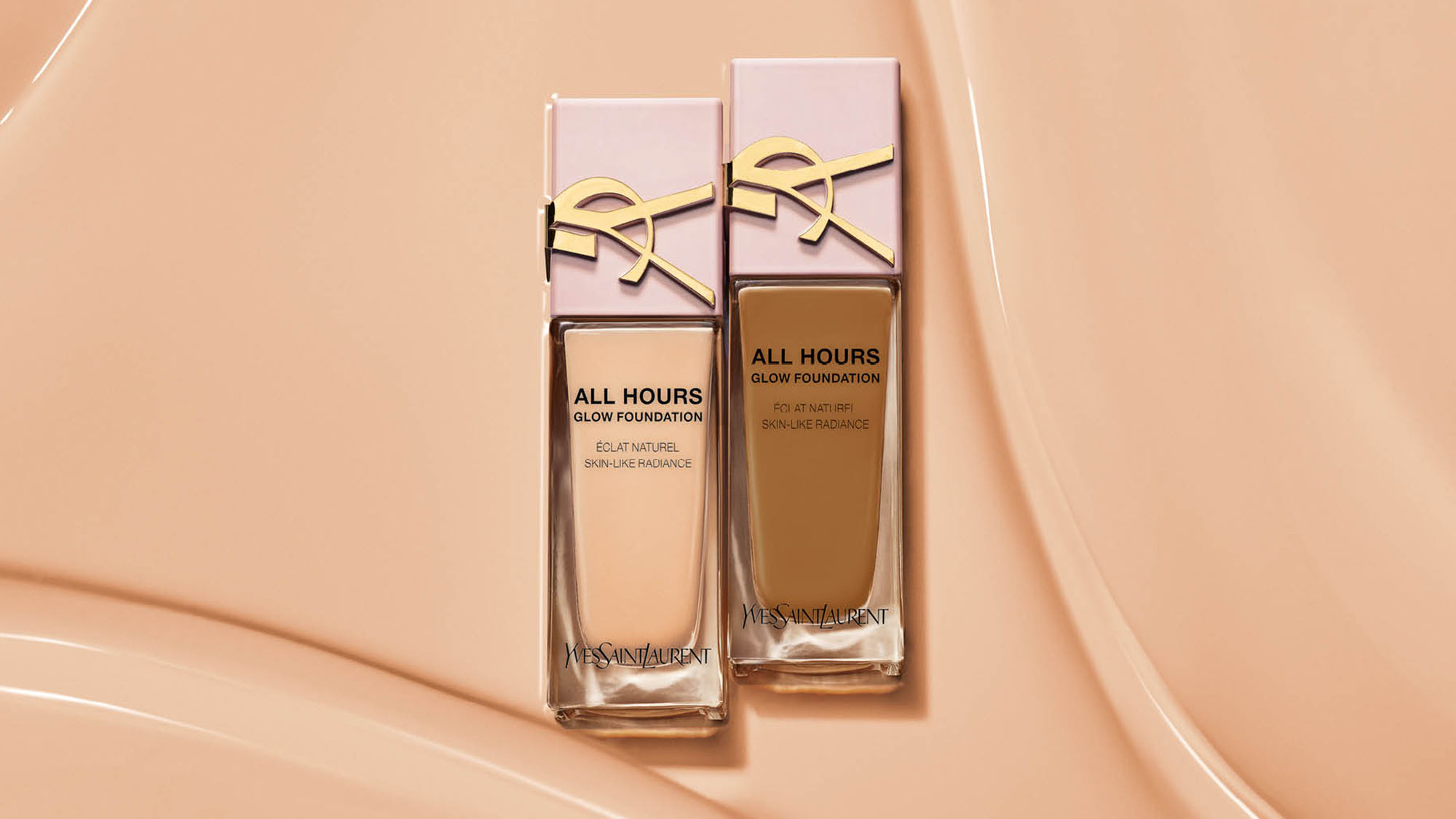 Two bottles of foundation with pink caps and gold detailing on a beige textured background.
