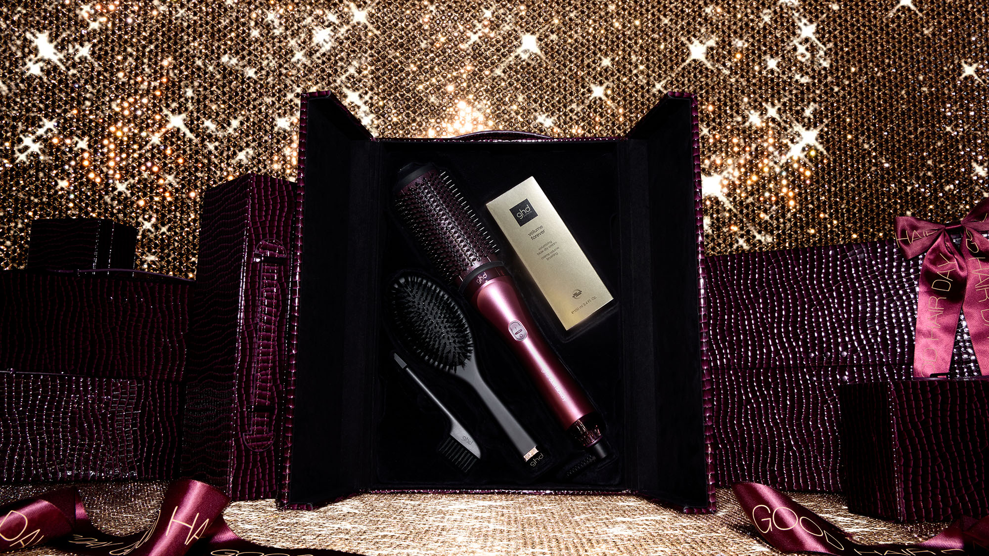 A gift box containing a hairdryer, brush, and product against a sparkling, golden background.