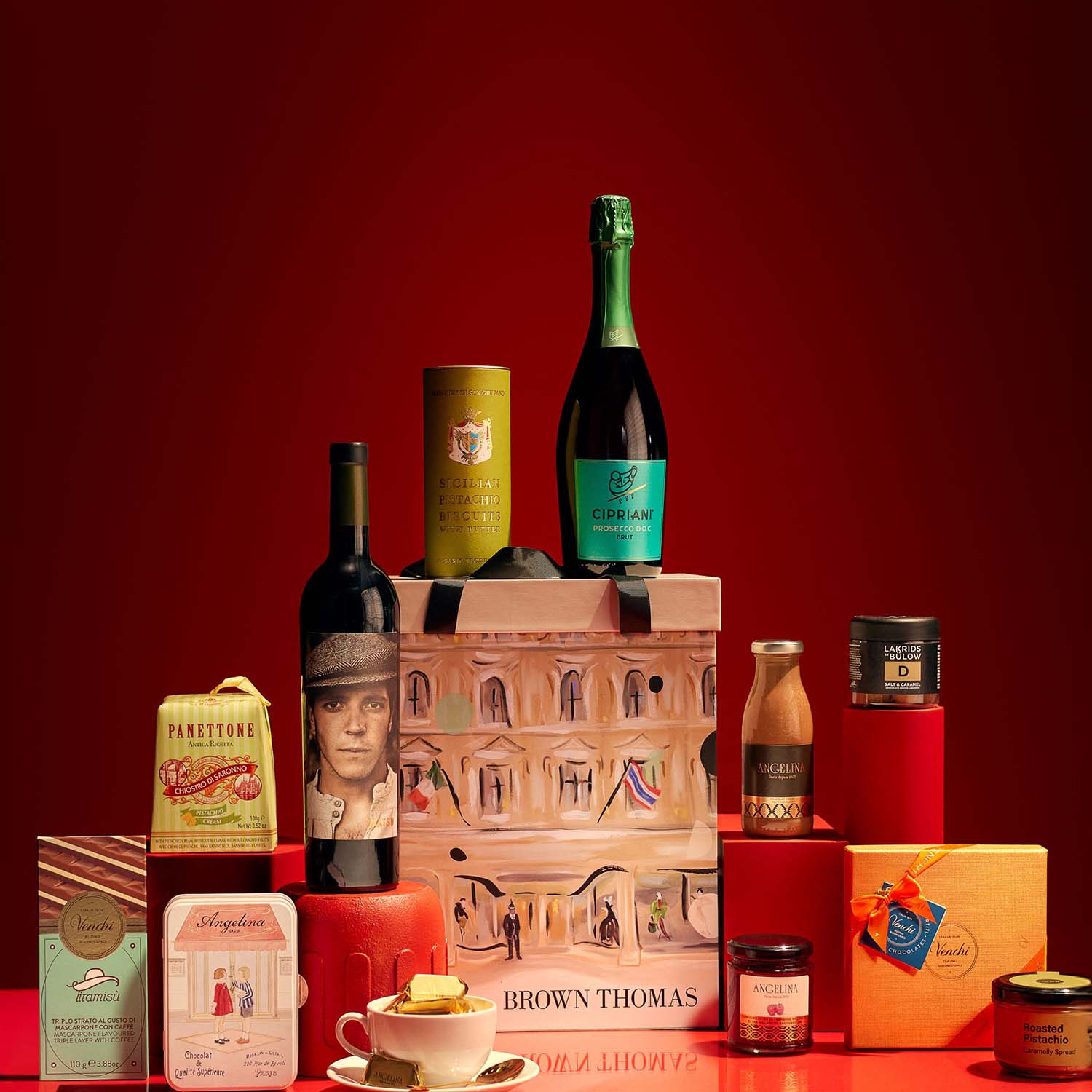 An assortment of gourmet food and drink items, including bottles, tins, and boxes, arranged on a red background.