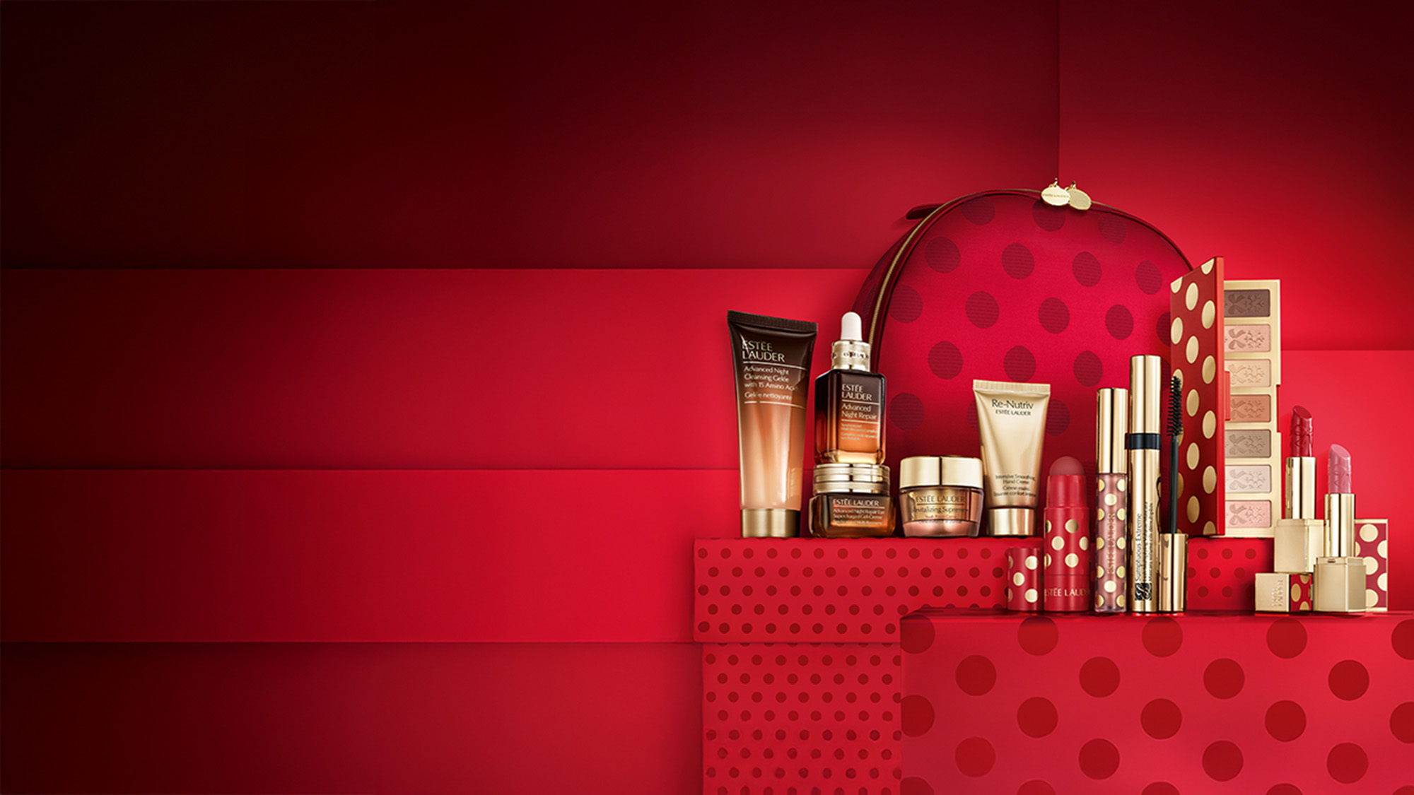 A collection of skincare and makeup products displayed on red polka-dotted boxes with a matching cosmetic bag.