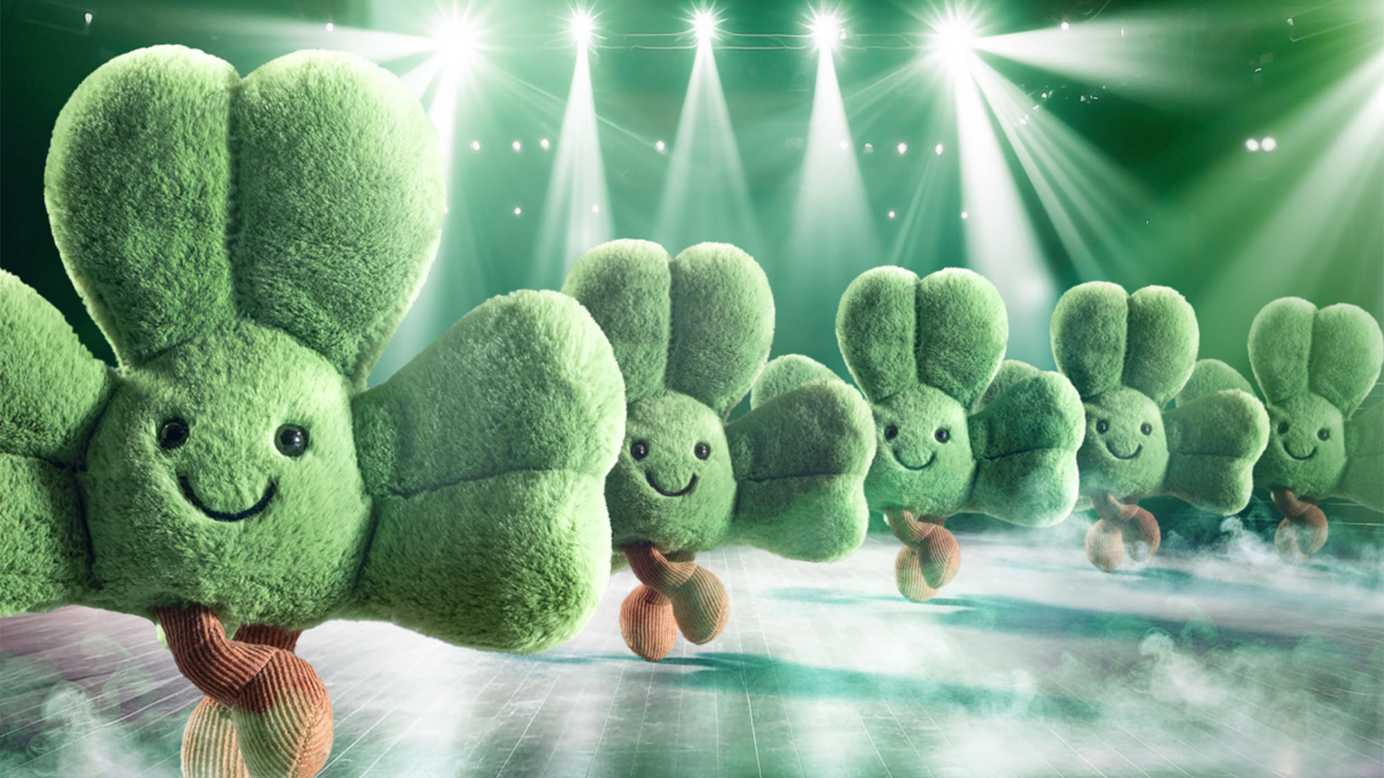 Cheerful, plush four-leaf clover characters dance on a stage under bright lights and fog effects.