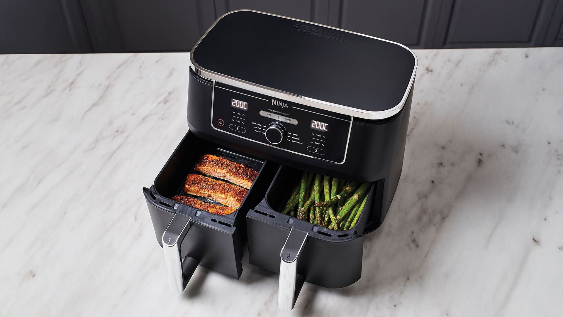 Black dual-basket air fryer on a marble surface, cooking salmon and asparagus.