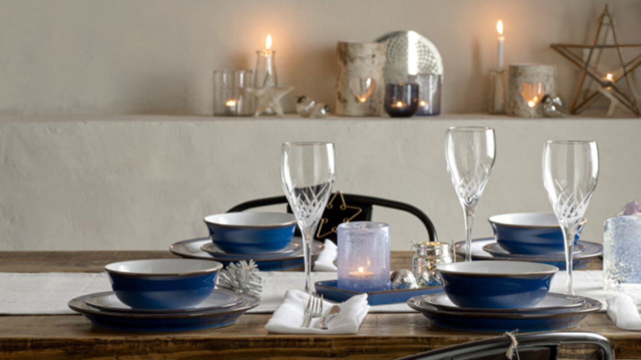 Elegant dining table set with blue dishes, champagne flutes, and candles. Background features glowing candles and star decor.