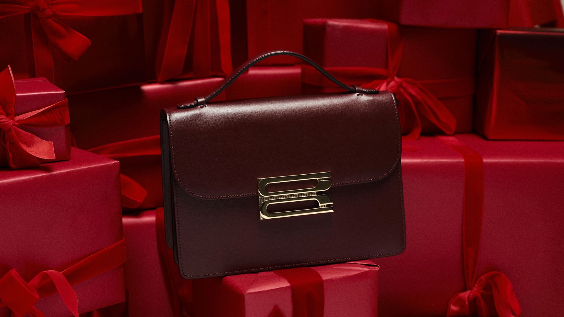 A dark brown handbag with a gold clasp sits among red gift boxes with bows.