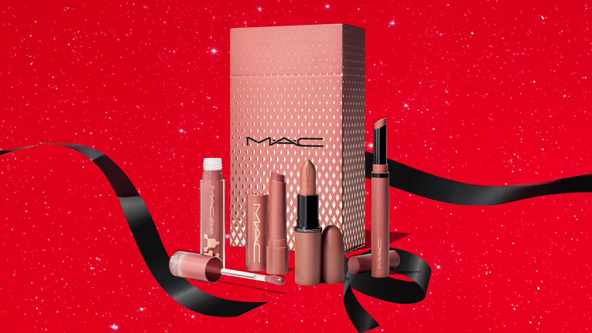 MAC makeup set with nude-toned lip products and elegant packaging against a glittery red background with black ribbon accents.