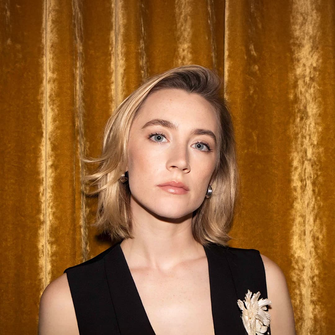 Saoirse Ronan wearing a black sleeveless top, standing in front of a gold curtain.
