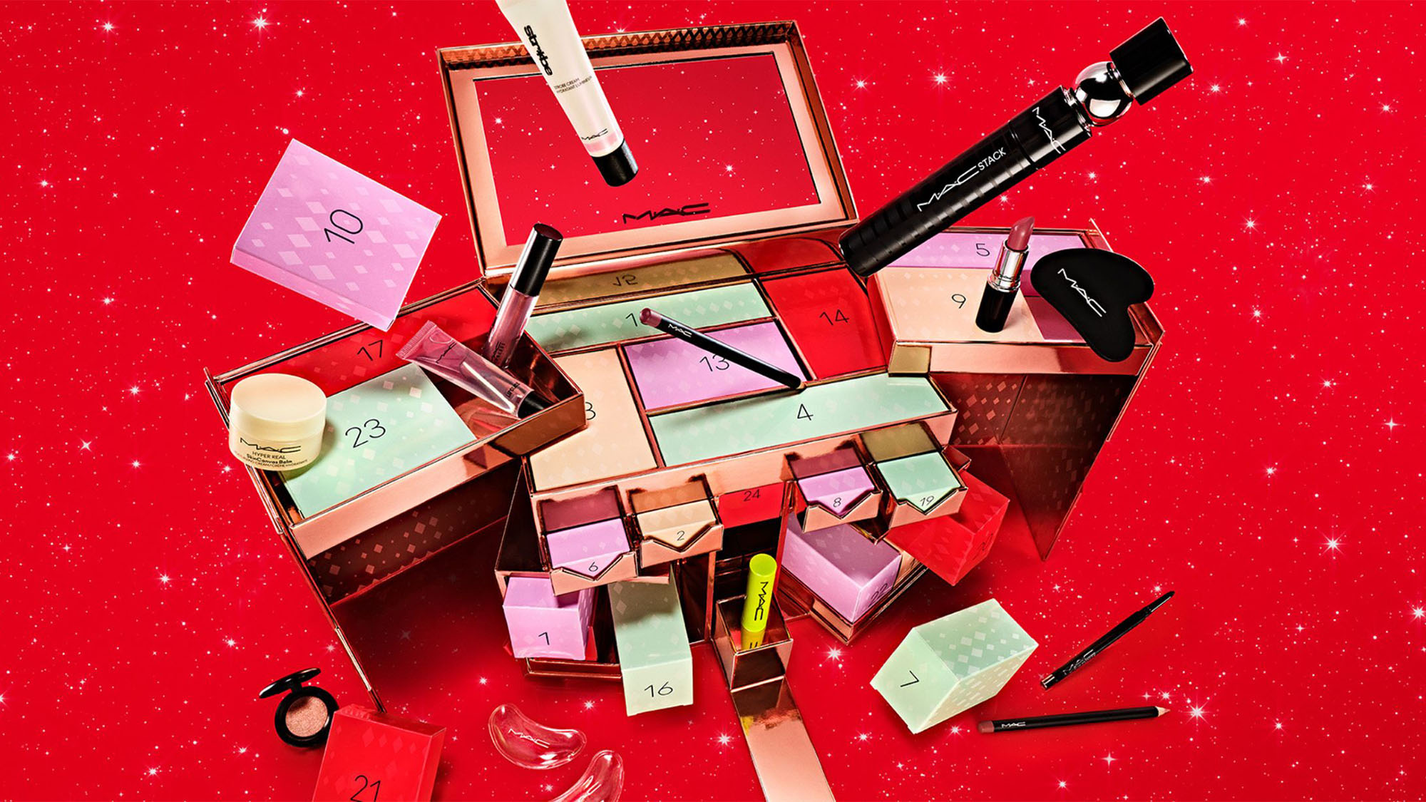 A MAC cosmetics advent calendar with makeup items arranged on a red glittery background.