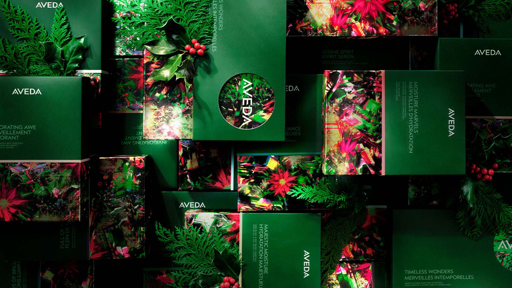 A collection of Aveda gift boxes featuring festive green and floral designs, with red berries and foliage accents.