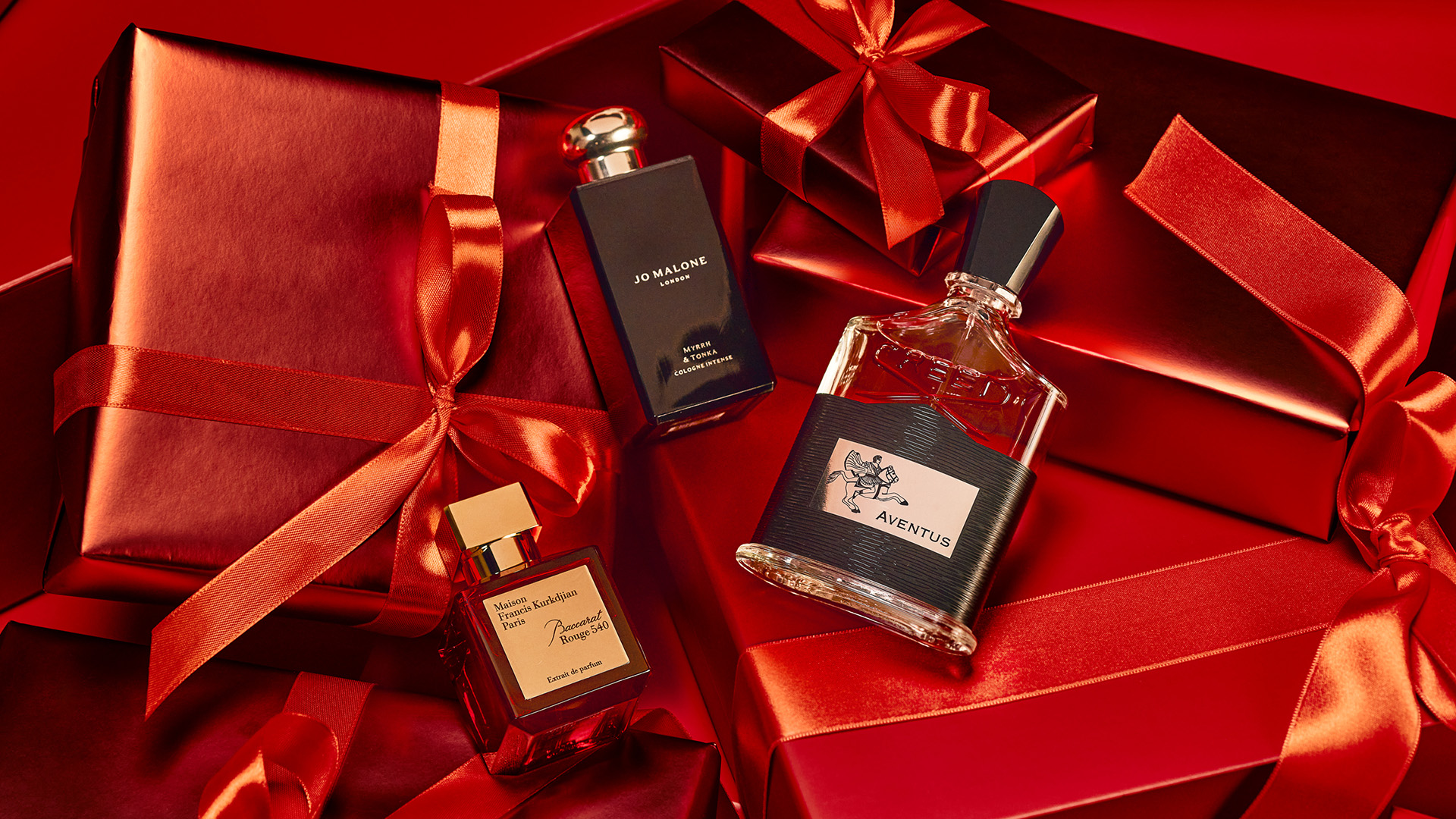 Perfume bottles arranged on and around red gift boxes with ribbons.