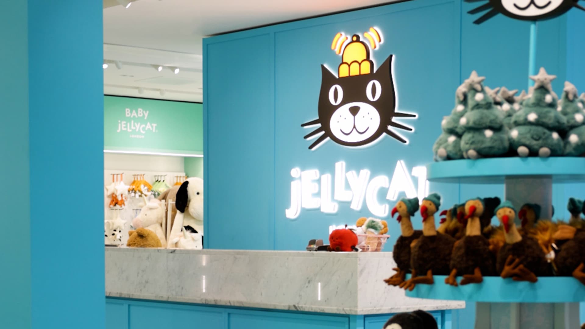 A retail display featuring Jellycat plush toys, with a bright blue theme and a prominent sign of a cat above the brand name.