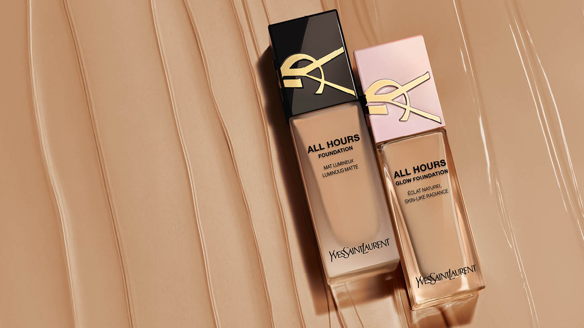 Two YSL All Hours foundations with gold logo caps on a streaked beige background.
