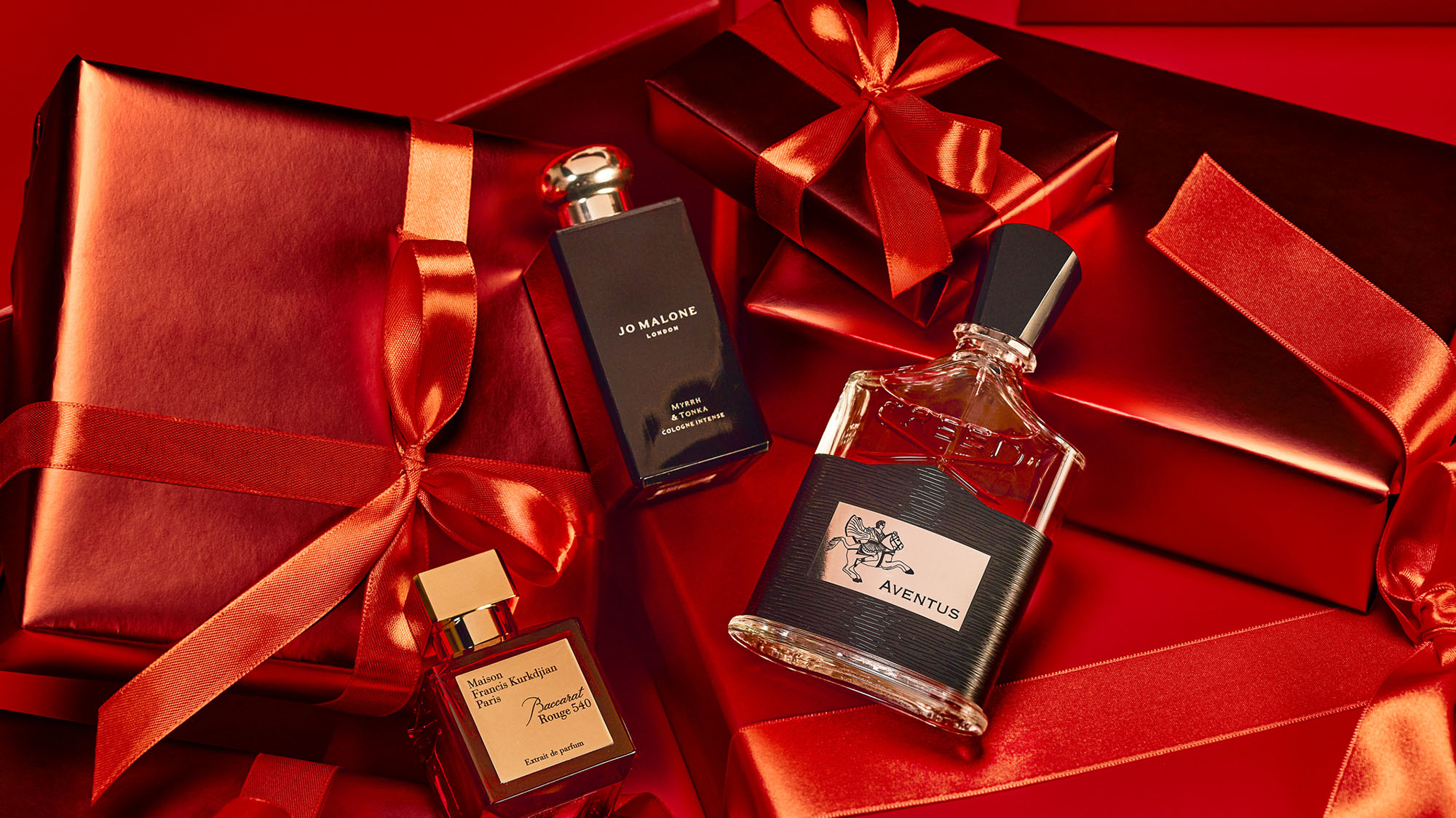 Perfume bottles surrounded by red wrapped gift boxes with ribbons on a red background.