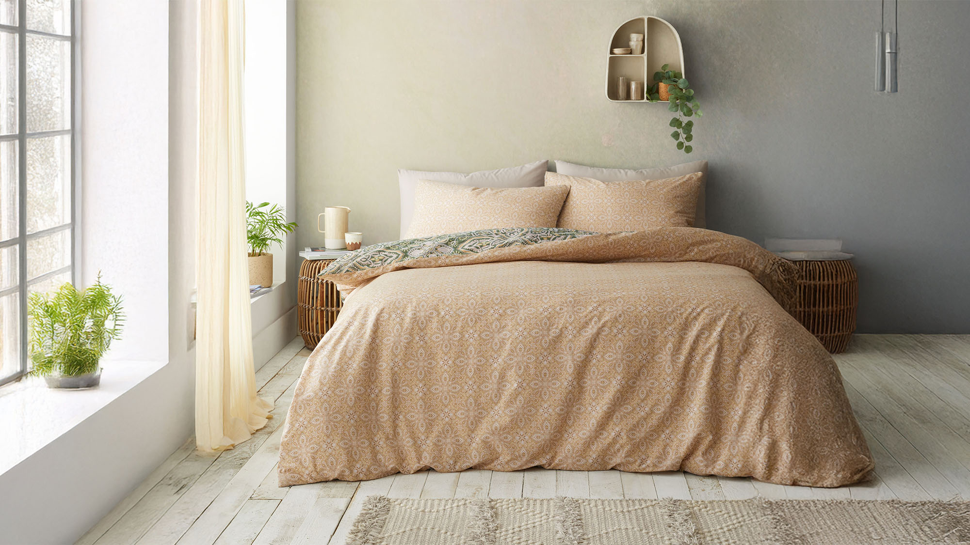 Cozy bedroom with a beige patterned bedspread, gray pillows, a small shelf with plants, and natural light from a window.