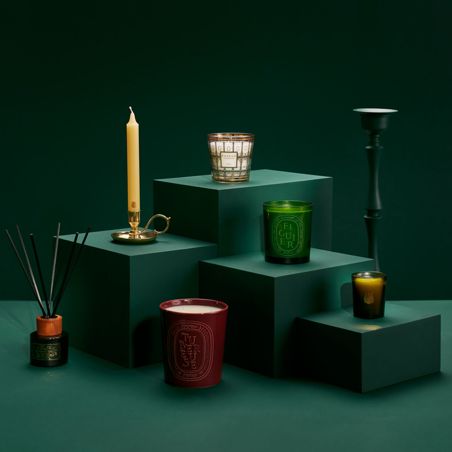 Assorted candles and diffusers displayed on green platforms against a dark green background.