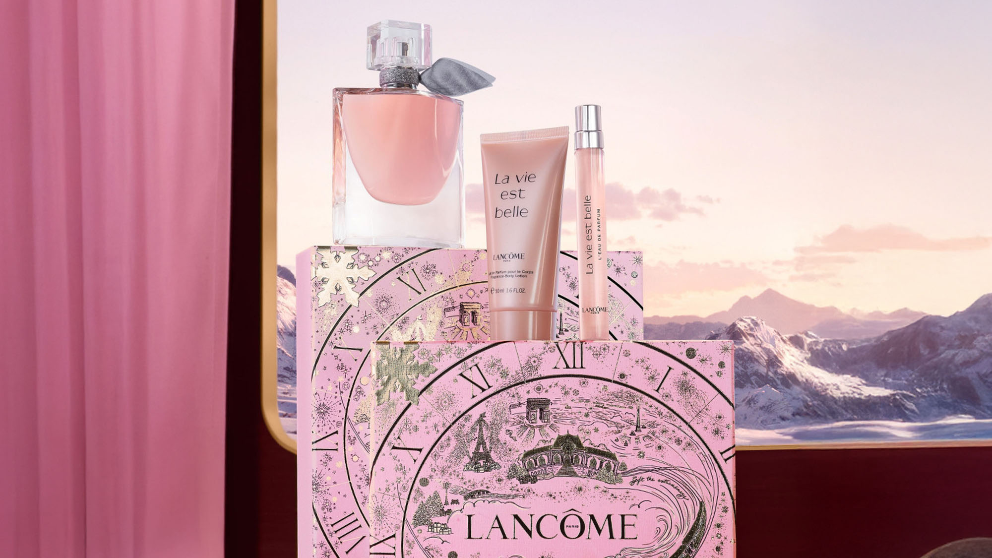 Lancôme perfume set with pink and gold packaging against a mountain backdrop.