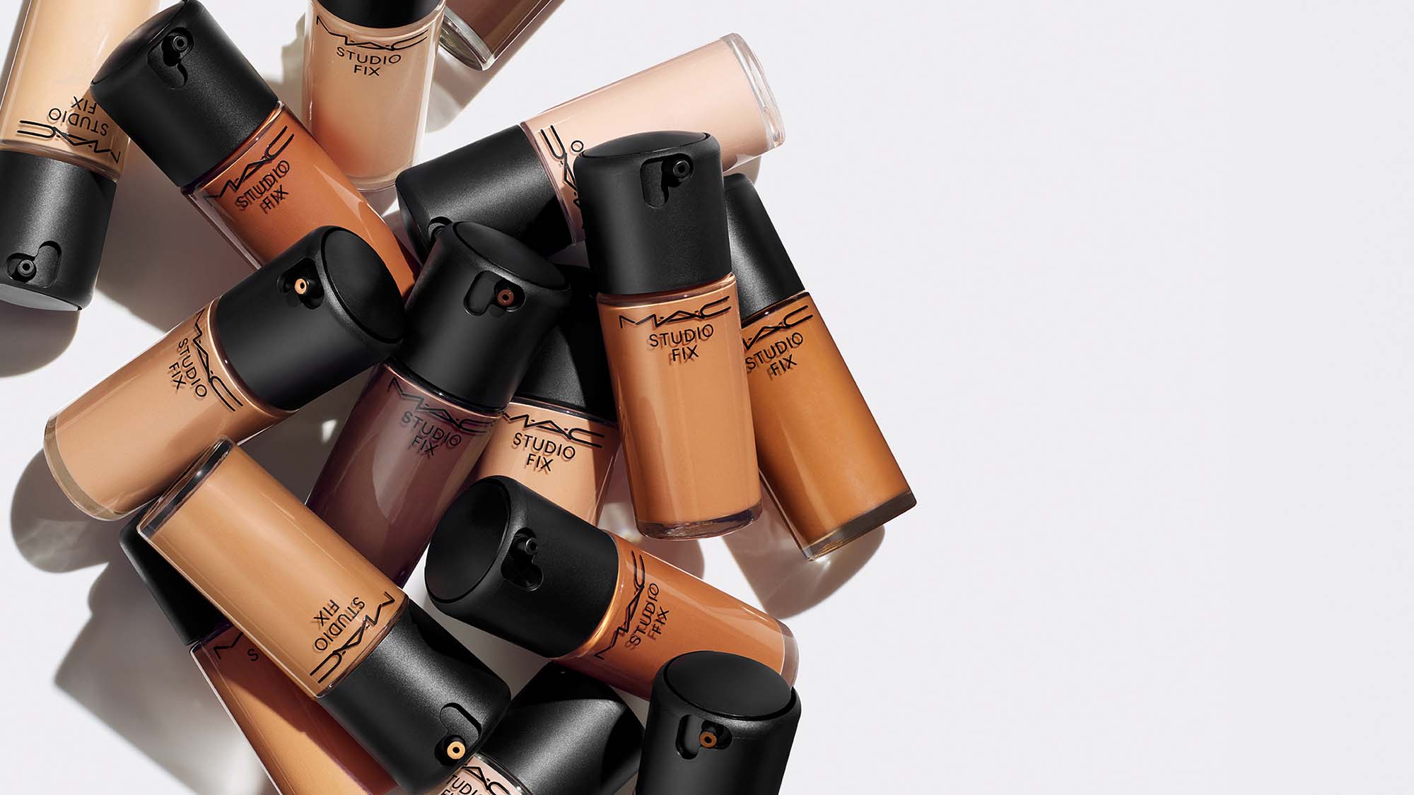 A set of MAC cosmetics, including spray, foundation, powder, and concealer, displayed against a light turquoise background with sparkles.