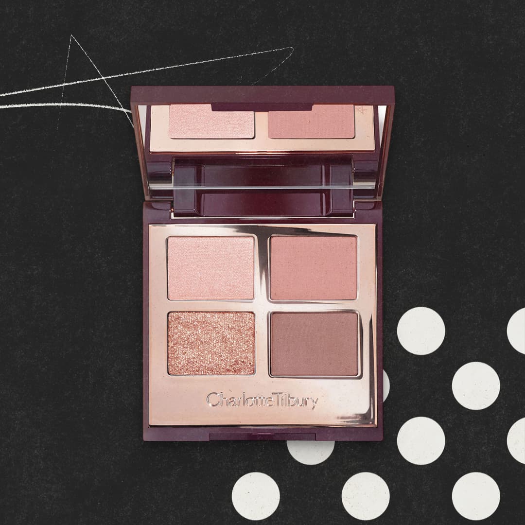 A makeup palette with four shades of eyeshadow in pink and brown tones on a dark background with white dots.