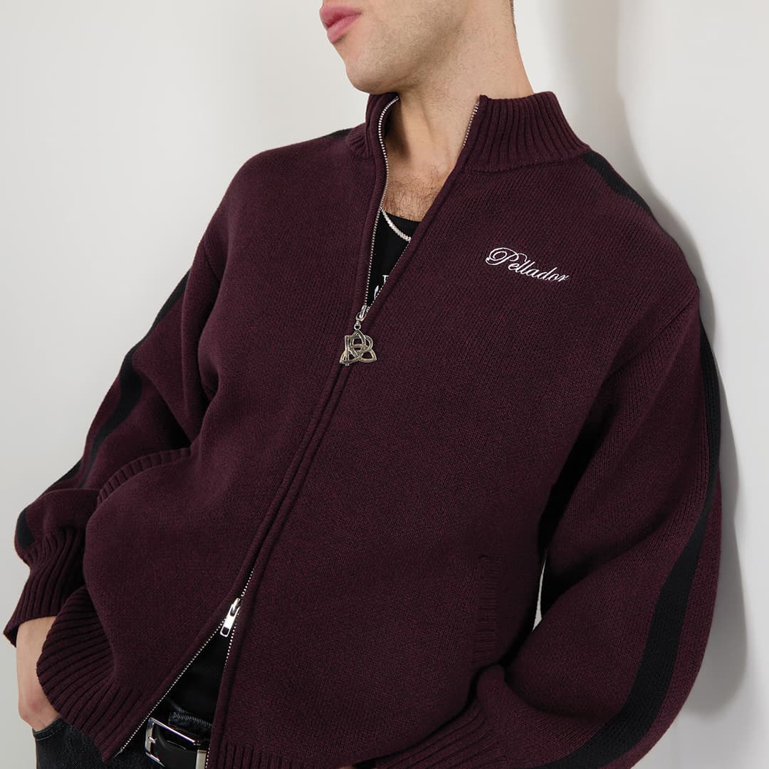 Person wearing a maroon zip-up sweater with a black stripe and embroidered text on the chest.