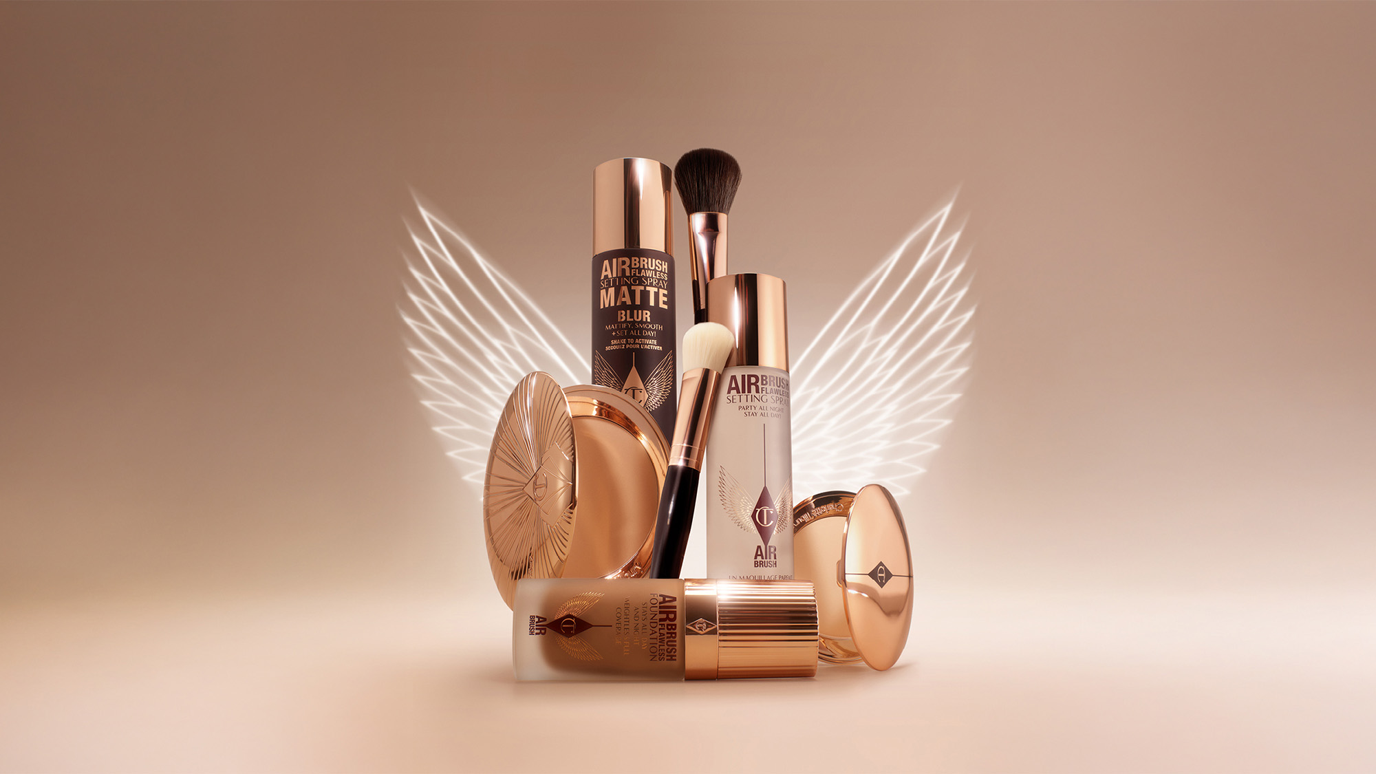 Collection of makeup products with rose gold packaging and winged design in the background.