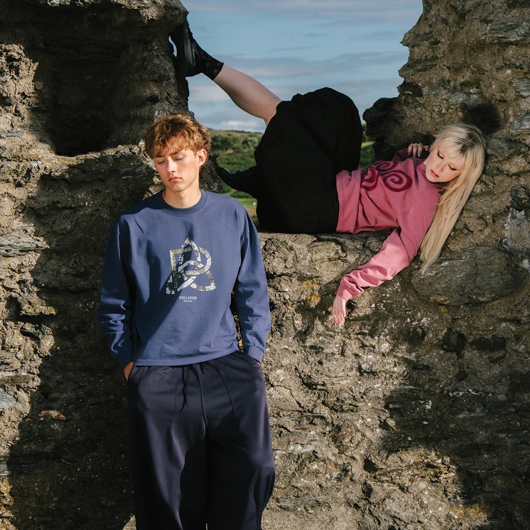 Two people in casual clothing pose among rocky ruins, one person leaning against a wall while the other reclines with legs elevated.