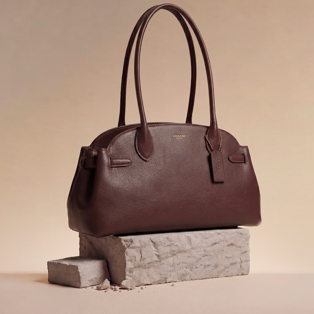 A brown leather handbag sits elegantly on a textured stone block against a beige background.