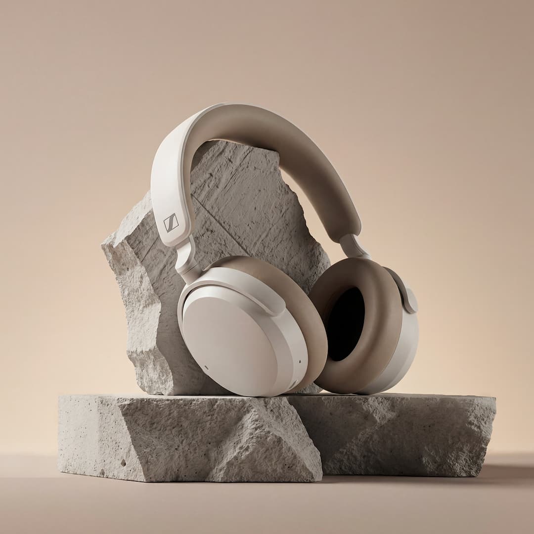 White and beige headphones displayed on stone blocks against a neutral background.