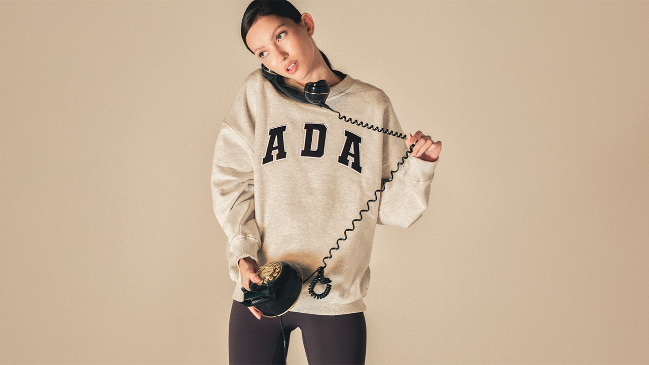 A person in a beige 'ADA' sweatshirt uses a vintage rotary phone.