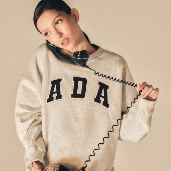 A person wearing a gray sweatshirt with 'ADA' printed on it is holding a vintage telephone receiver.