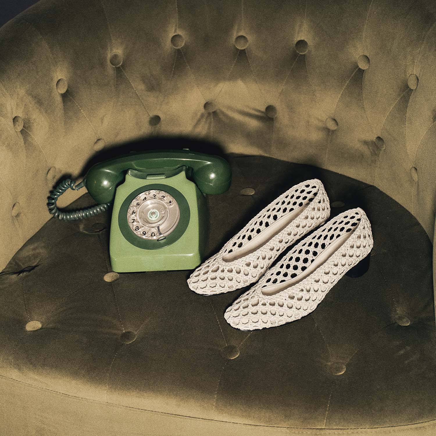 A green rotary phone and white mesh shoes on a green tufted chair.