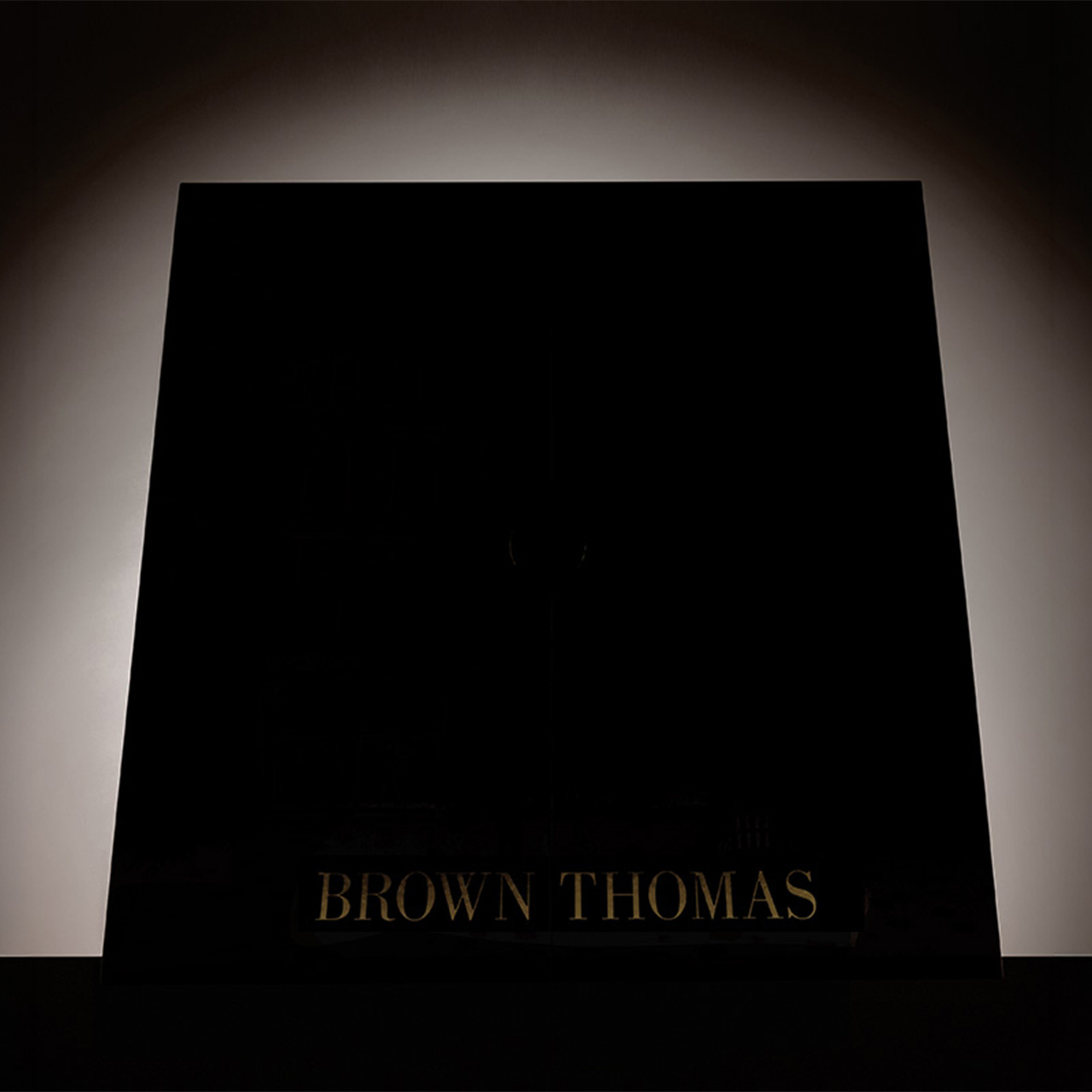 Black luxury shopping bag with Brown Thomas branding and soft spotlight lighting