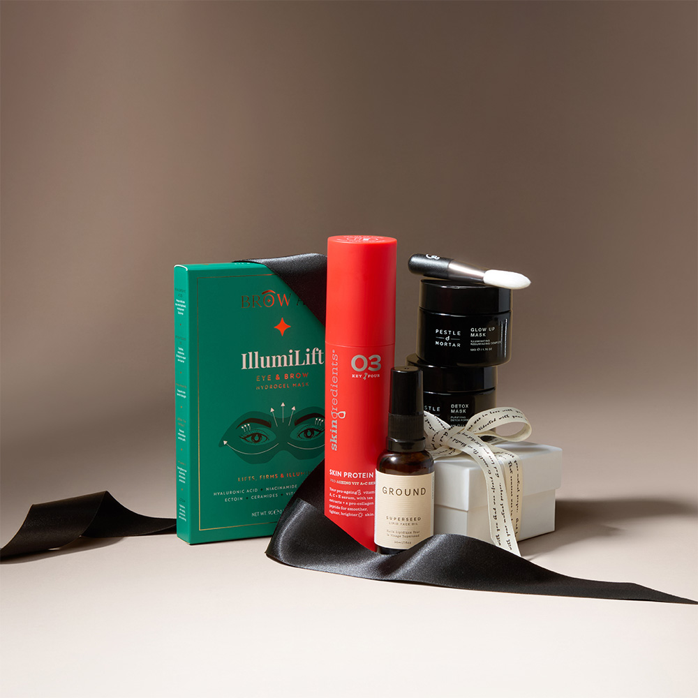 A collection of skincare and beauty products, including a red bottle, a green box, a white wrapped gift, and small jars, with a black ribbon.