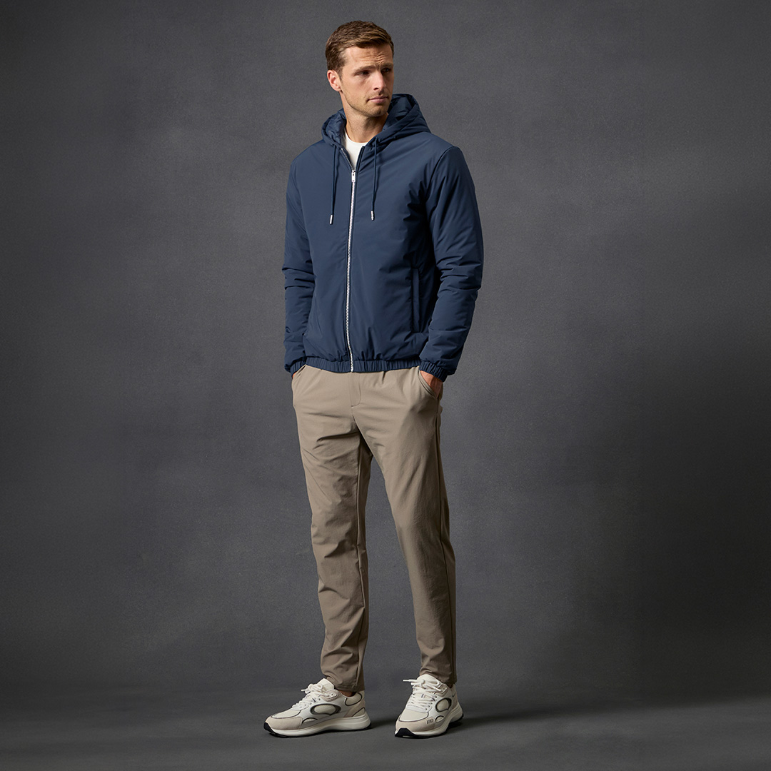 Man wearing navy hooded jacket and beige trousers with white trainers, Arne everyday essentials collection